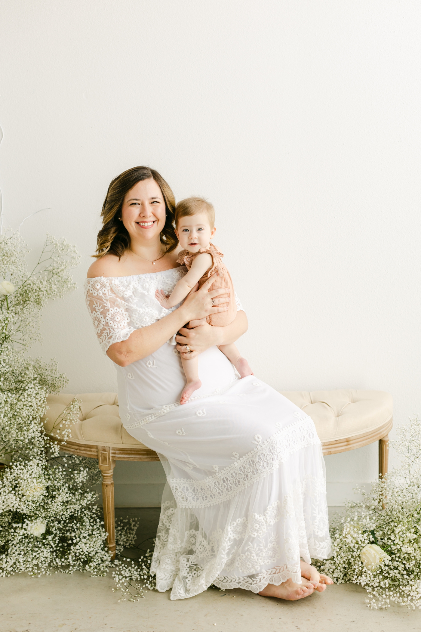 Mom in white lace maxi dress holding baby as they smile at the camera. Photo by Sana Ahmed Photography.