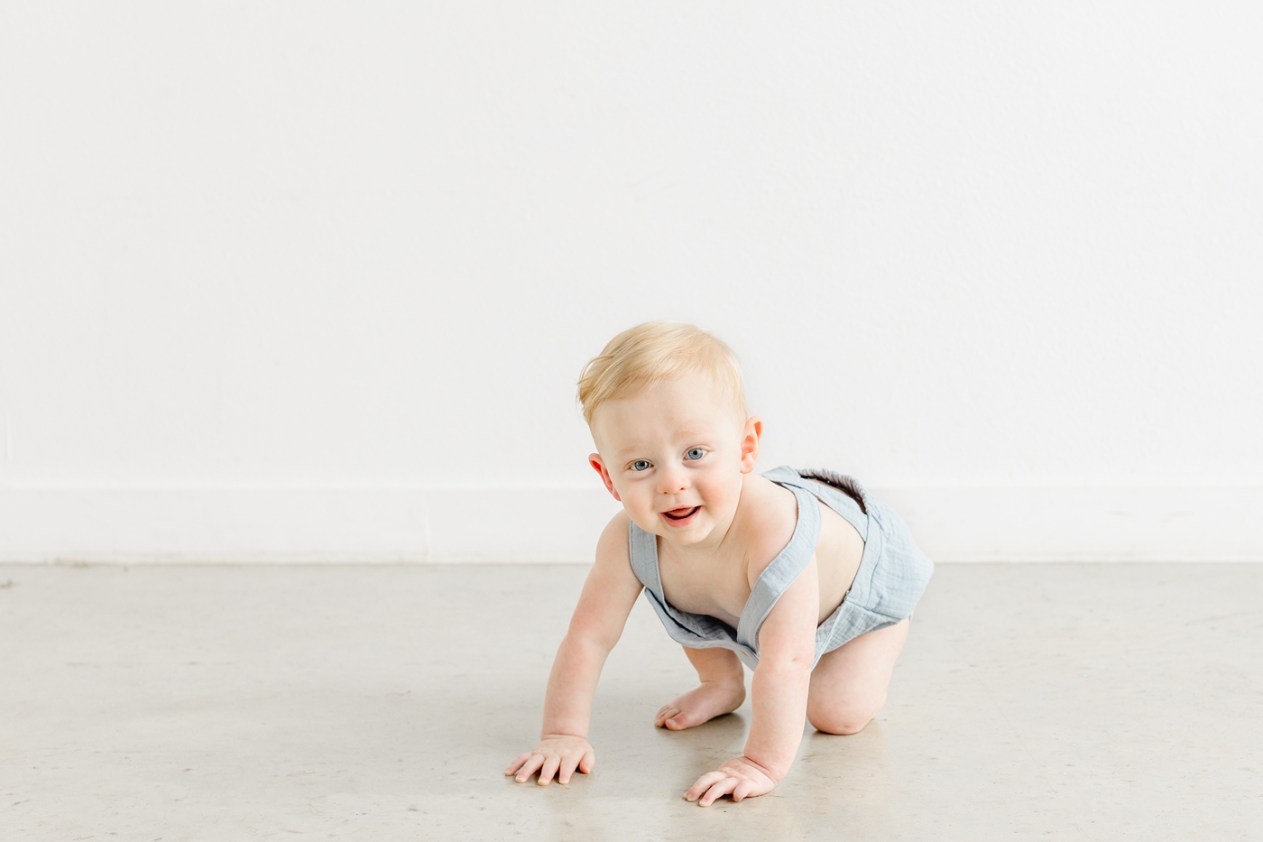 Baby boy in blue romper crawling during his one year milestone session with Sana Ahmed Photography.