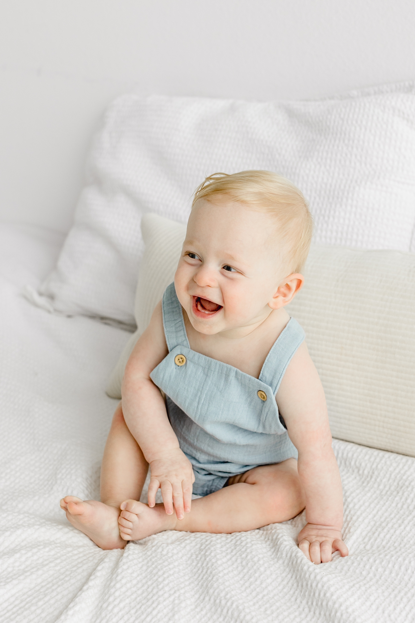 Smiling little boy in blue romper during first birthday milestone session. Photo by Sana Ahmed Photography.
