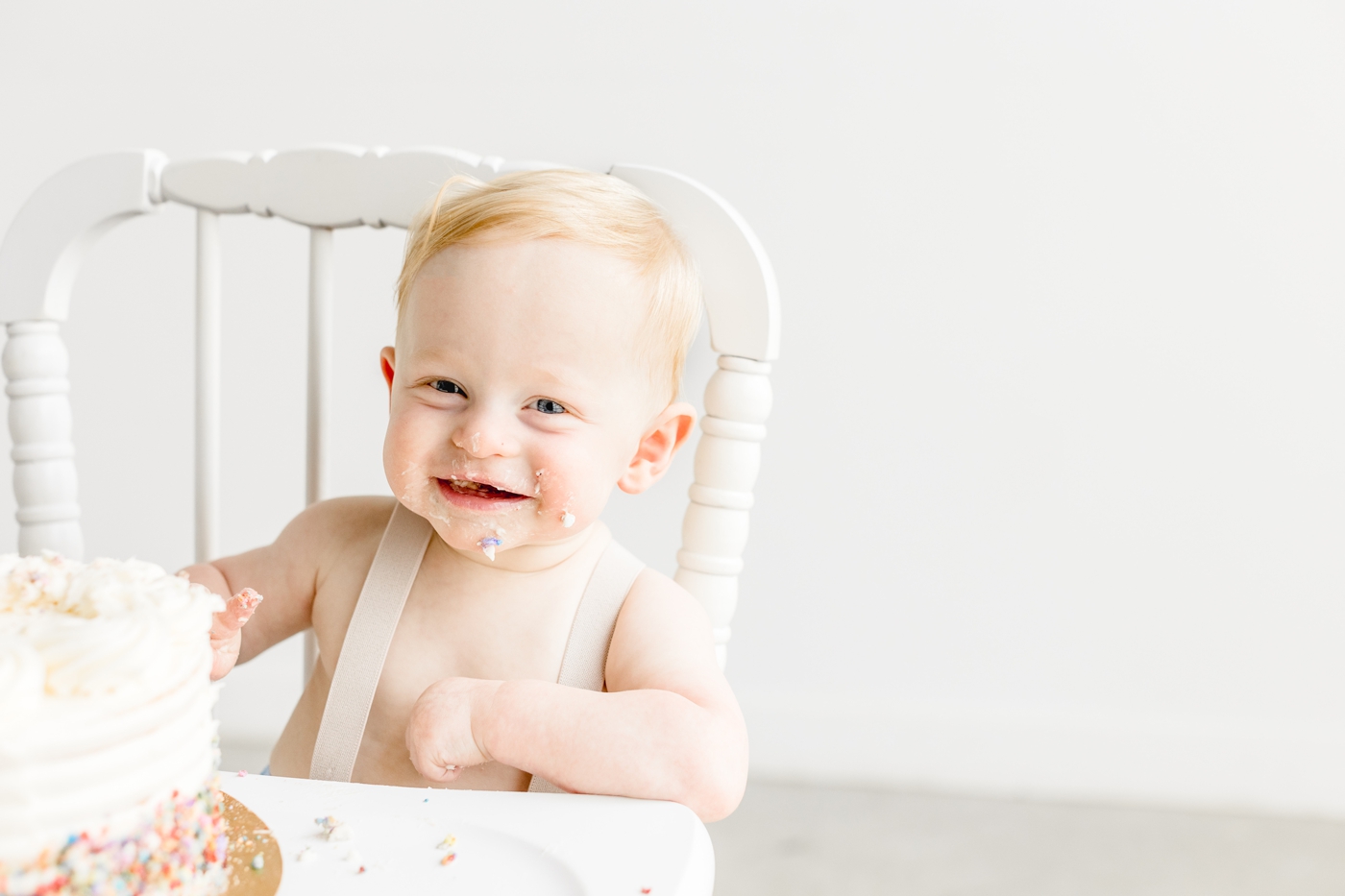 Smiling baby in white highchair during his first birthday cake smash session with Austin photographer, Sana Ahmed Photography.