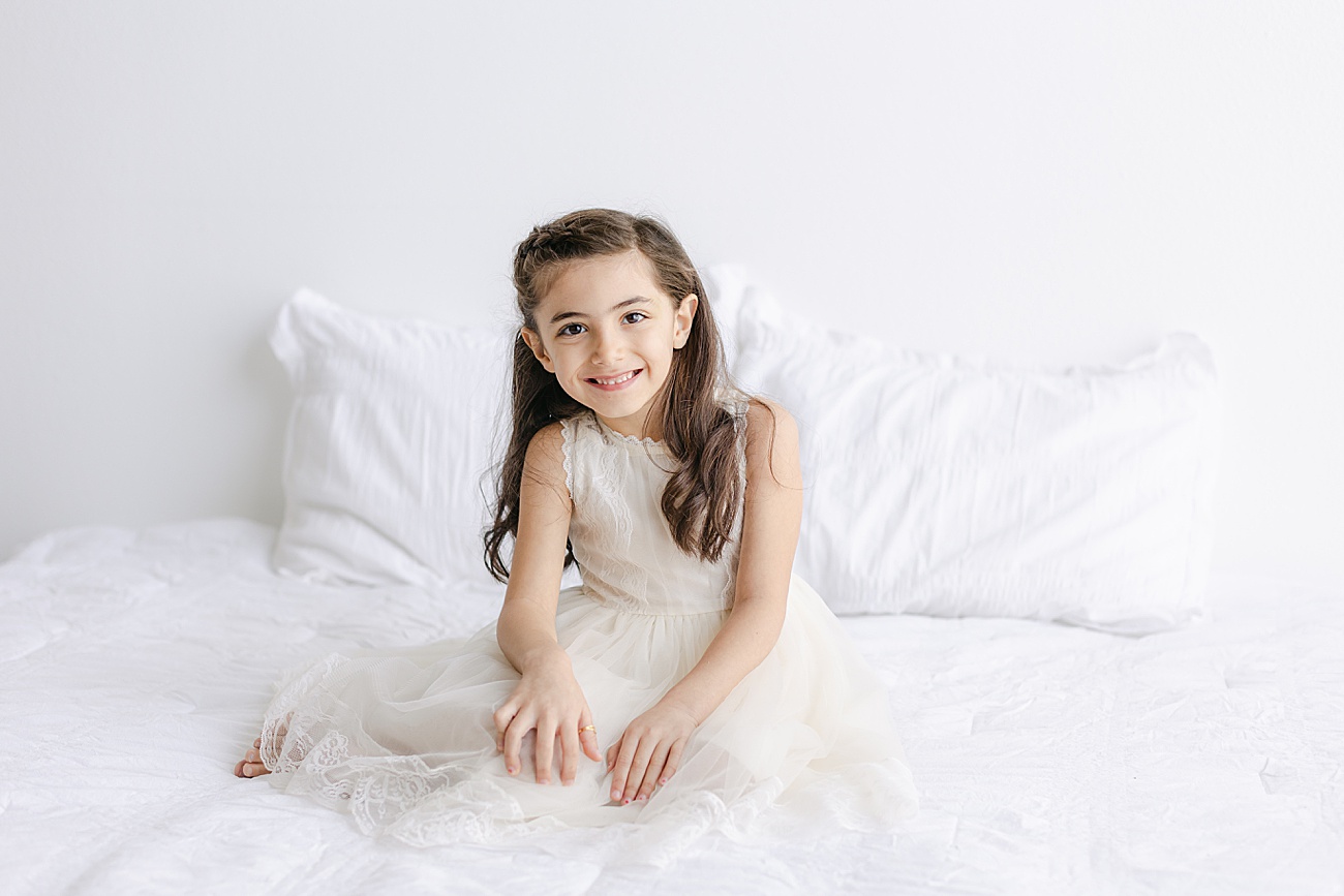 Big sister wearing off-white tulle dress as she smiles at the camera. Photo by Sana Ahmed Photography.