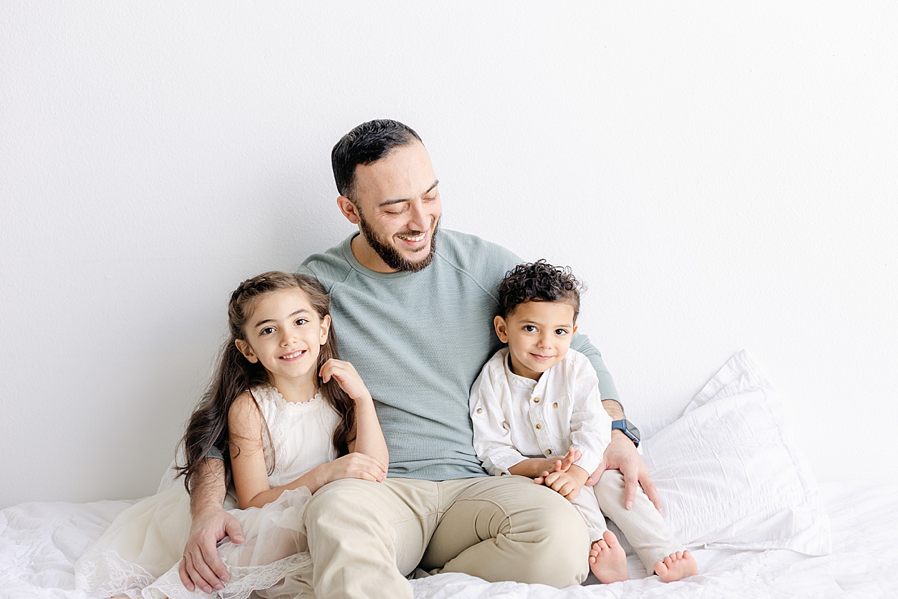 Dad sitting with kids on bed in studio. Photo by Sana Ahmed Photography.