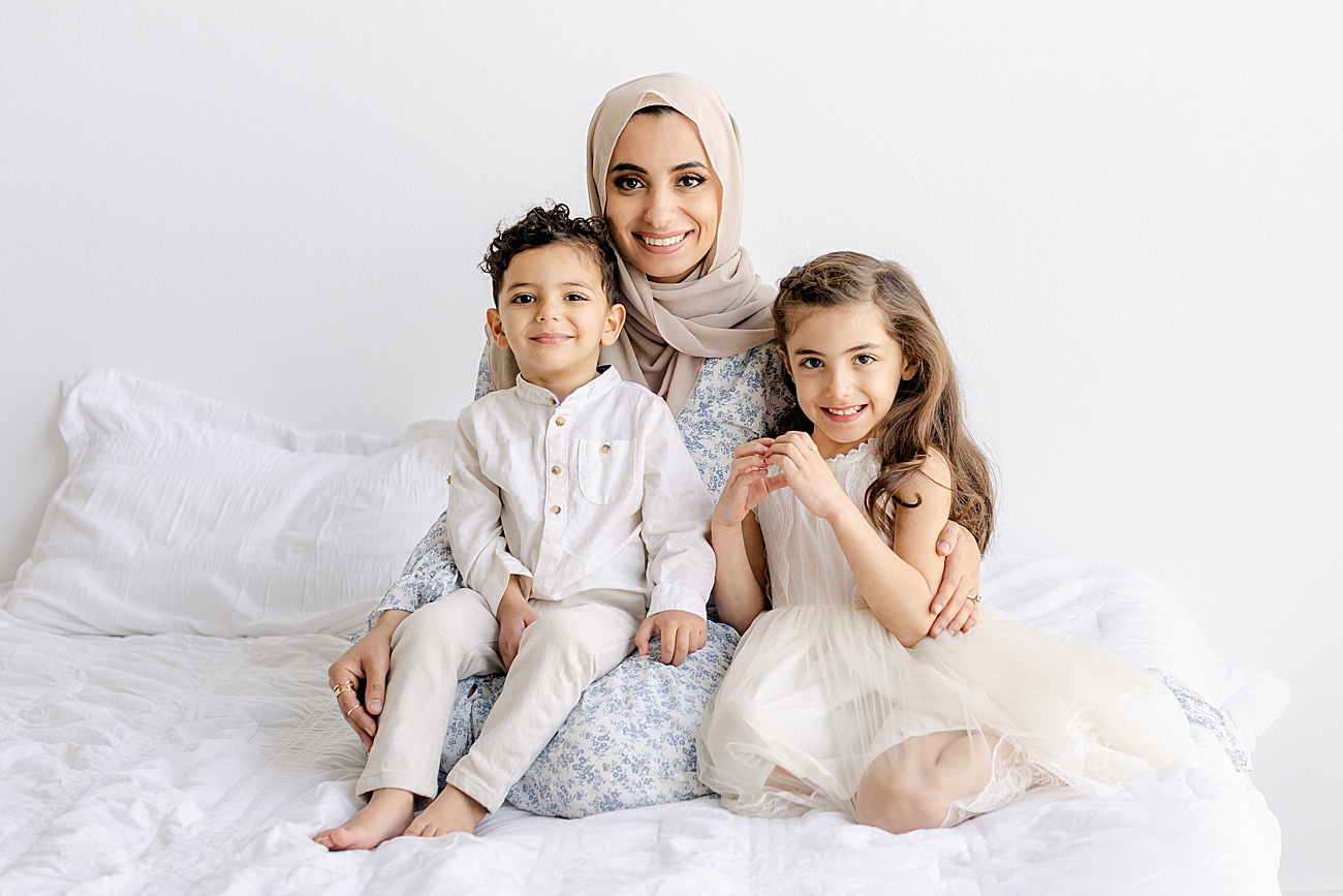 Mom wearing hijab smiling at camera with two children during family session in Austin, TX studio. Photo by Sana Ahmed Photography.