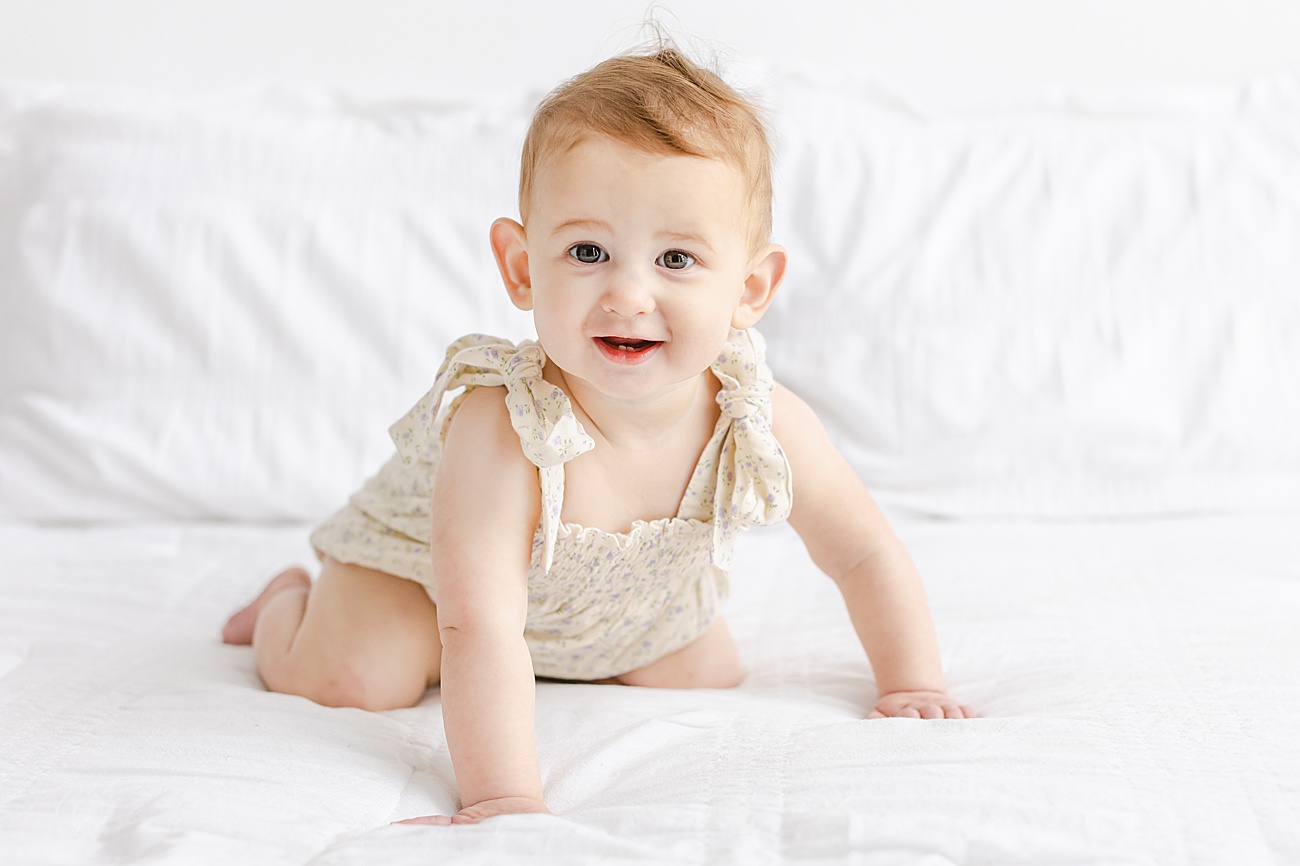 Little girl crawling on studio bed in floral romper. Photo by Sana Ahmed Photography.