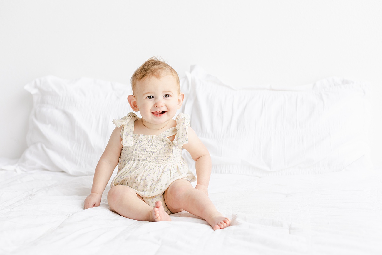 Happy baby grinning while sitting on bed in studio. Photo by Sana Ahmed Photography.
