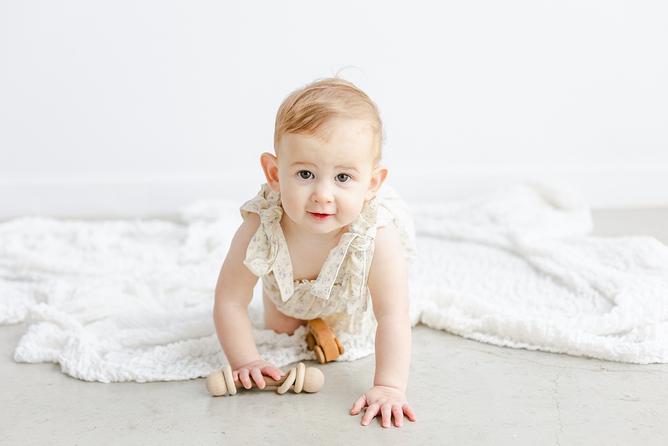 Little girl crawling on studio floor during first birthday session. 