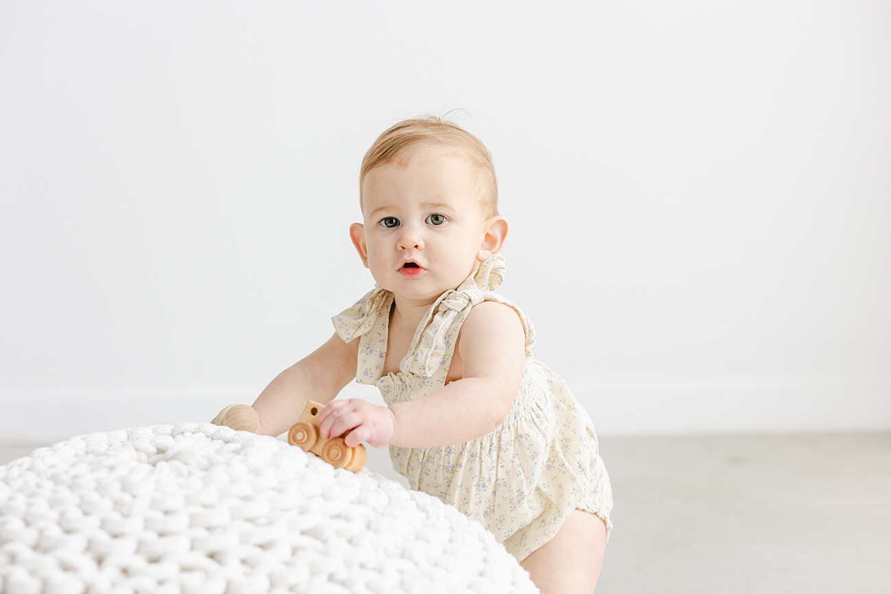 Little girl standing up against white knit pouf during first birthday session with Sana Ahmed Photography.