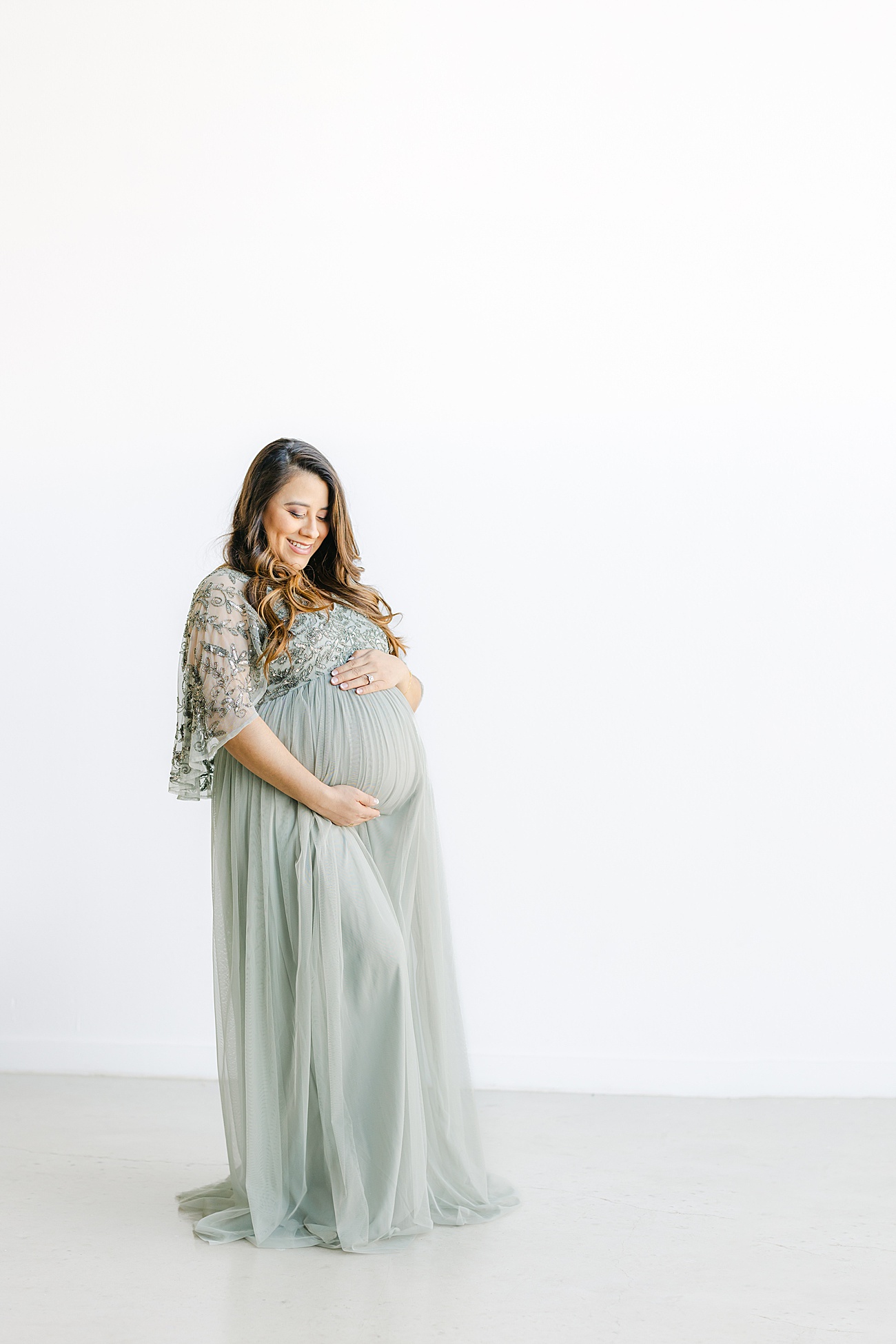 Mama-to-be wearing sage green maternity dress in studio maternity session for first baby. Photo by Sana Ahmed Photography.