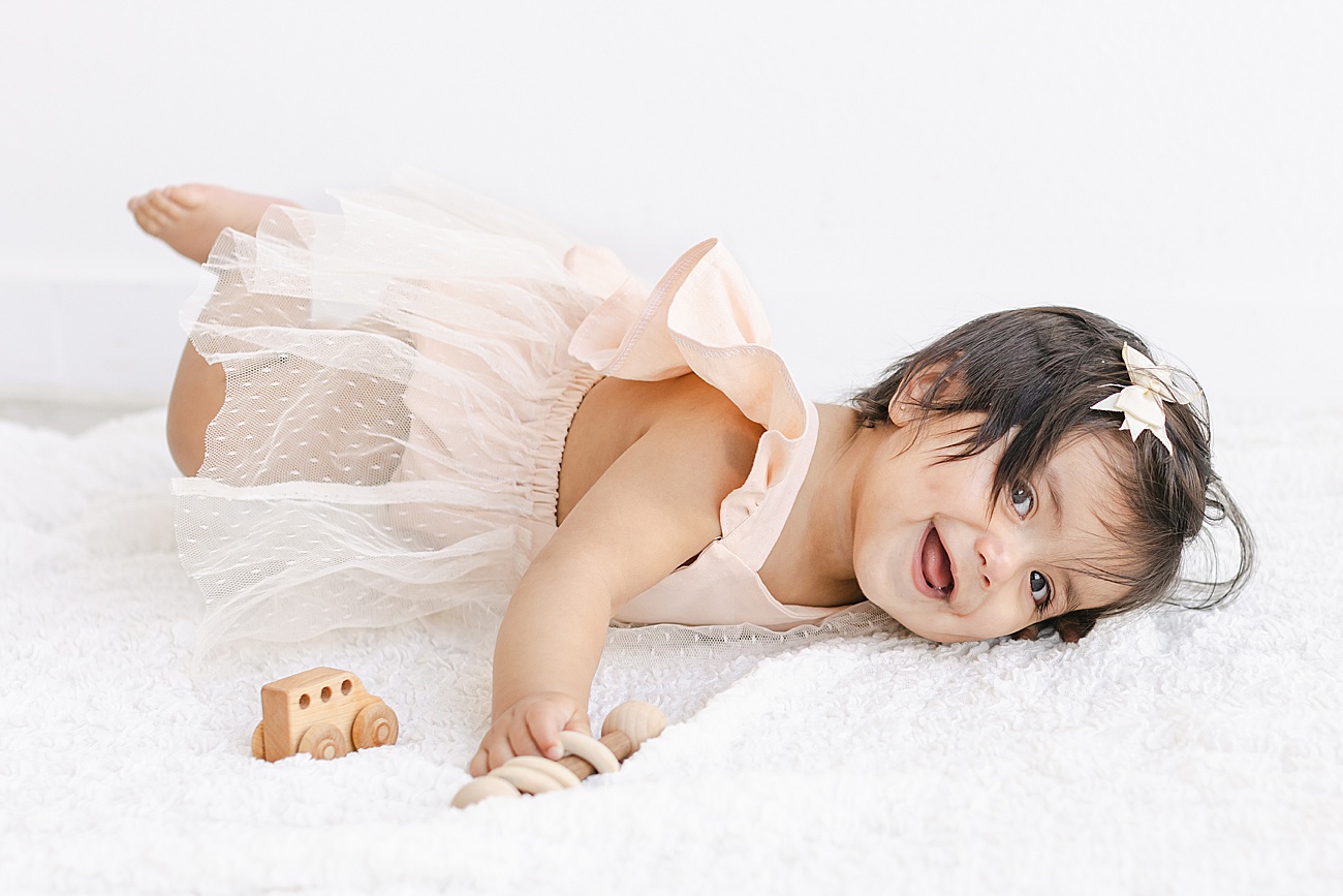 Sweet baby girl playing on studio bed during milestone session. Photo by Sana Ahmed Photography.