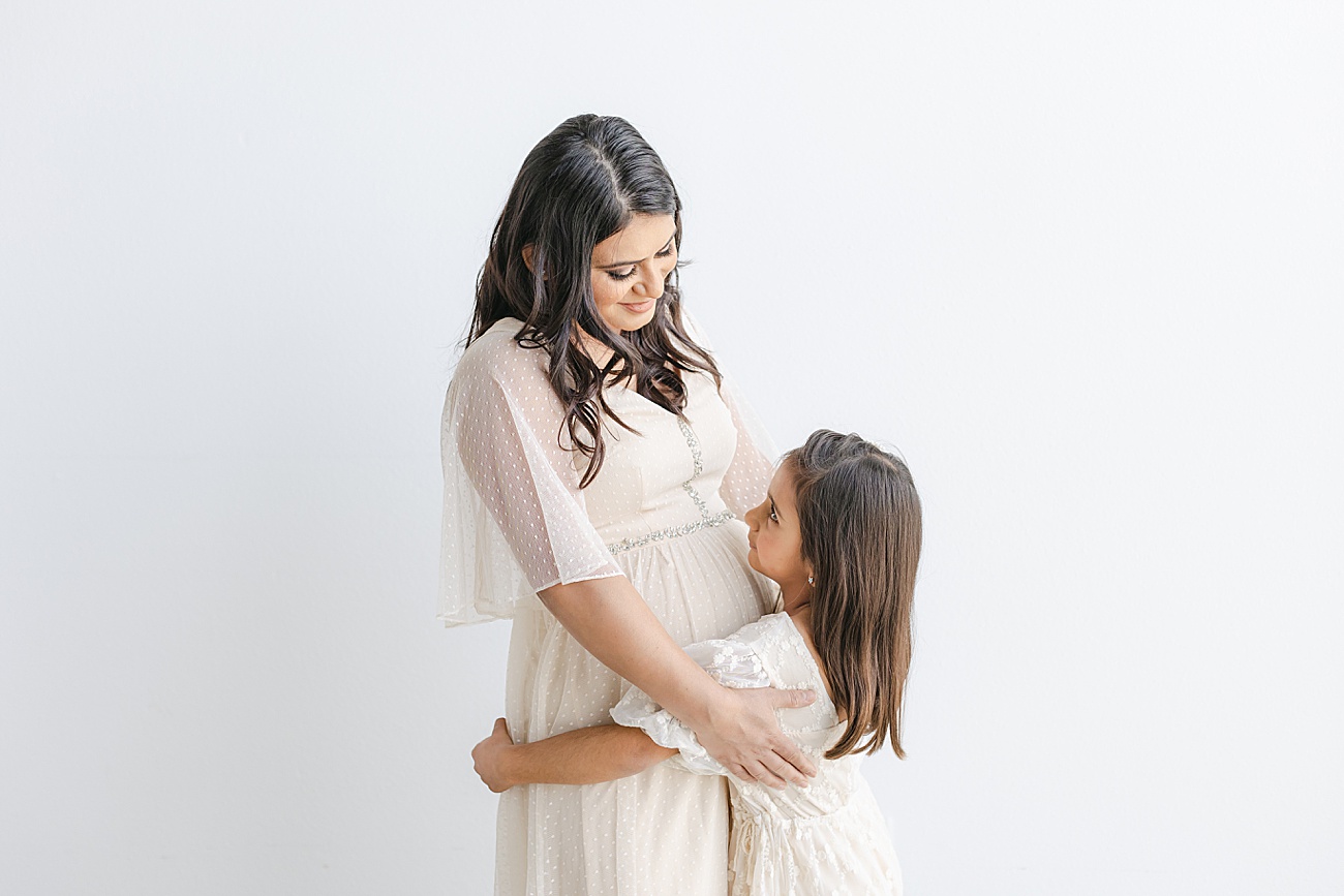 Mom and daughter dresses in neutral dresses as they hug. Photo by Sana Ahmed Photography.