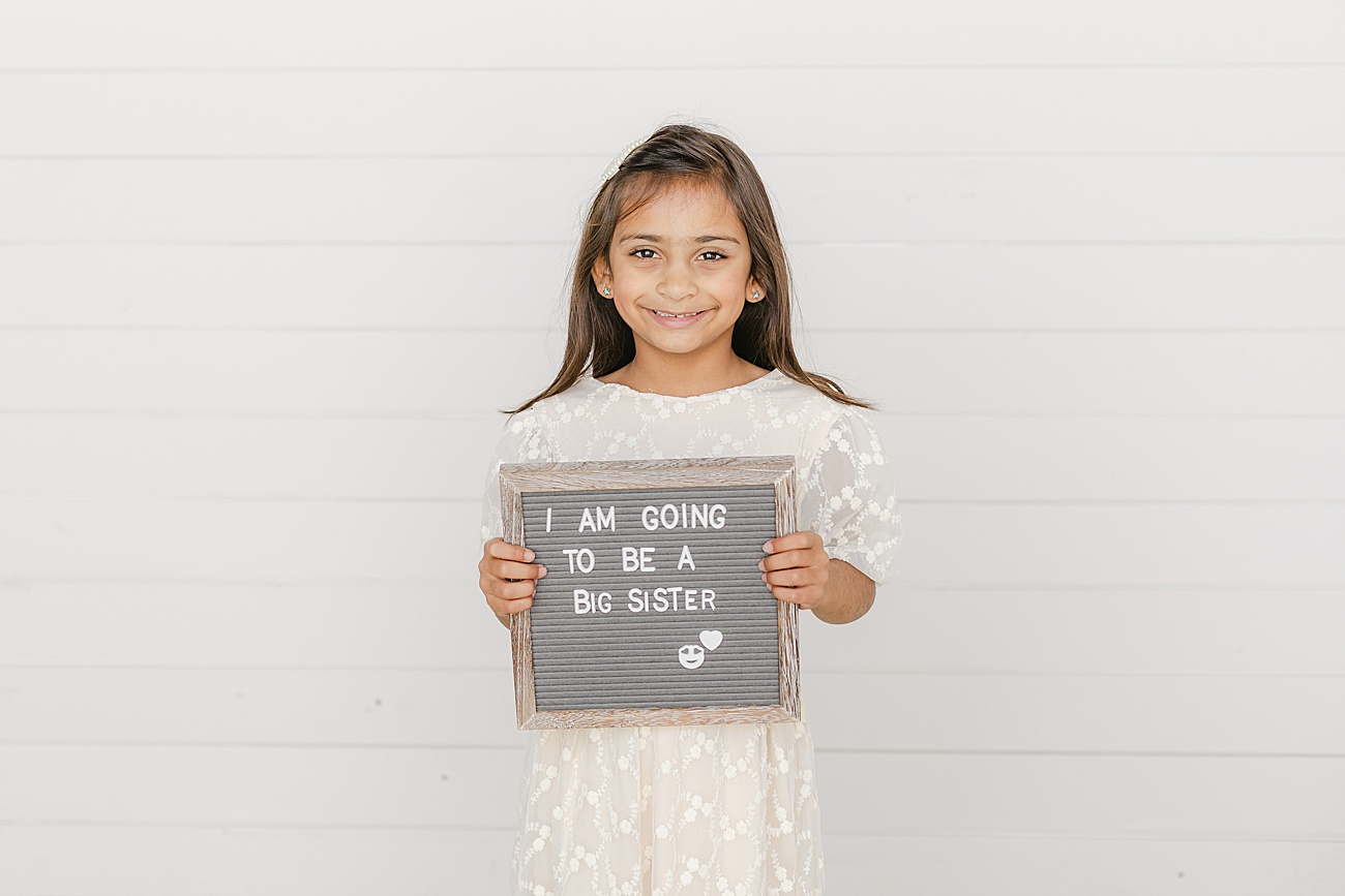Big sister holding letterboard. Photo by Sana Ahmed Photography.