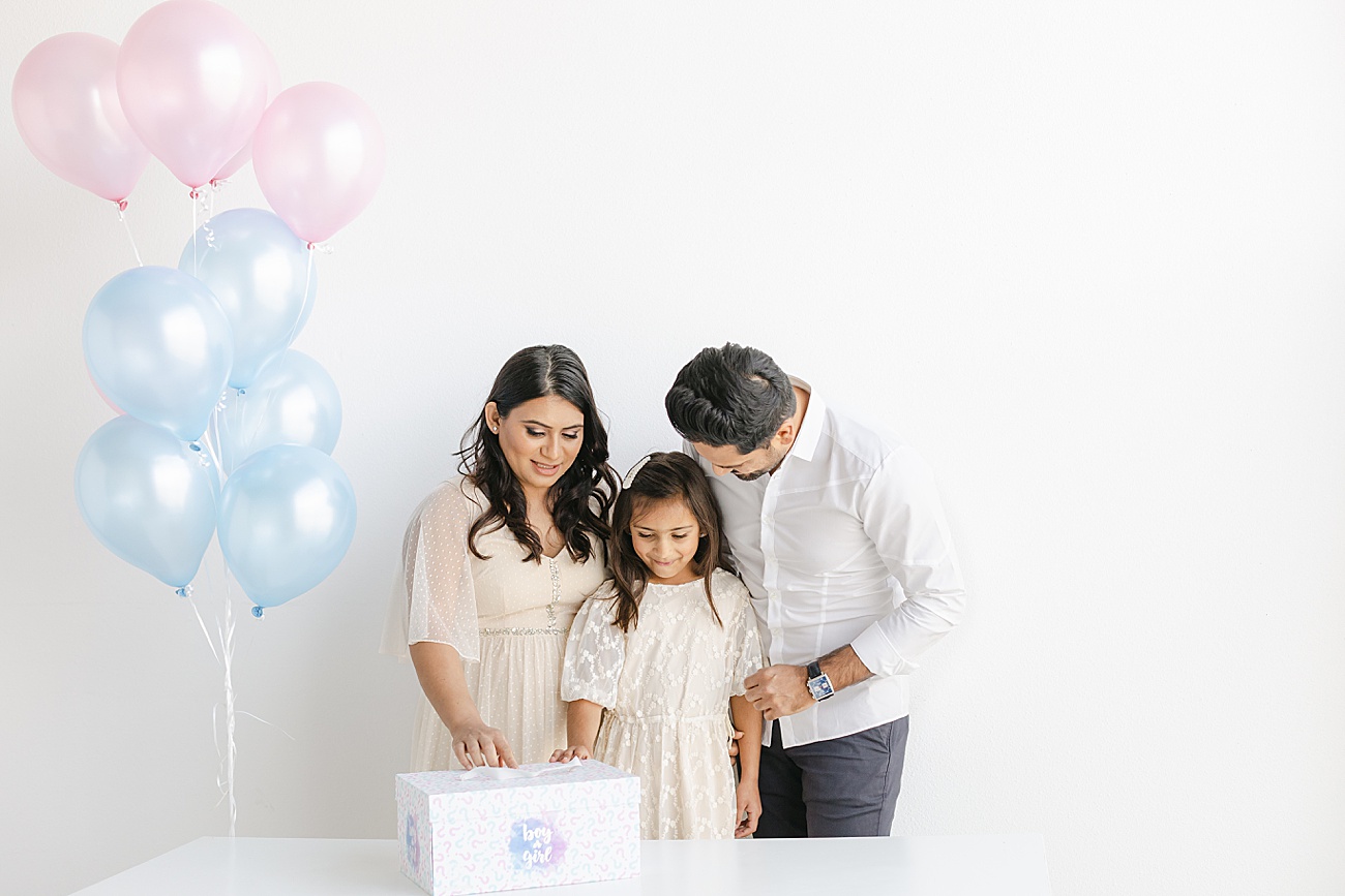 Big sister preparing to take lid off of baby gender reveal box during session with Sana Ahmed Photography.