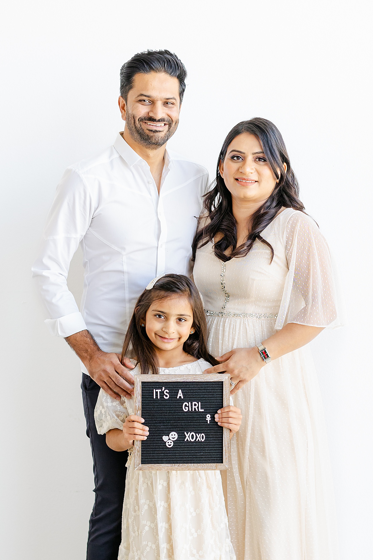 Portrait of family of three holding a letter board to announce baby number two is a girl. Photo by Sana Ahmed Photography.