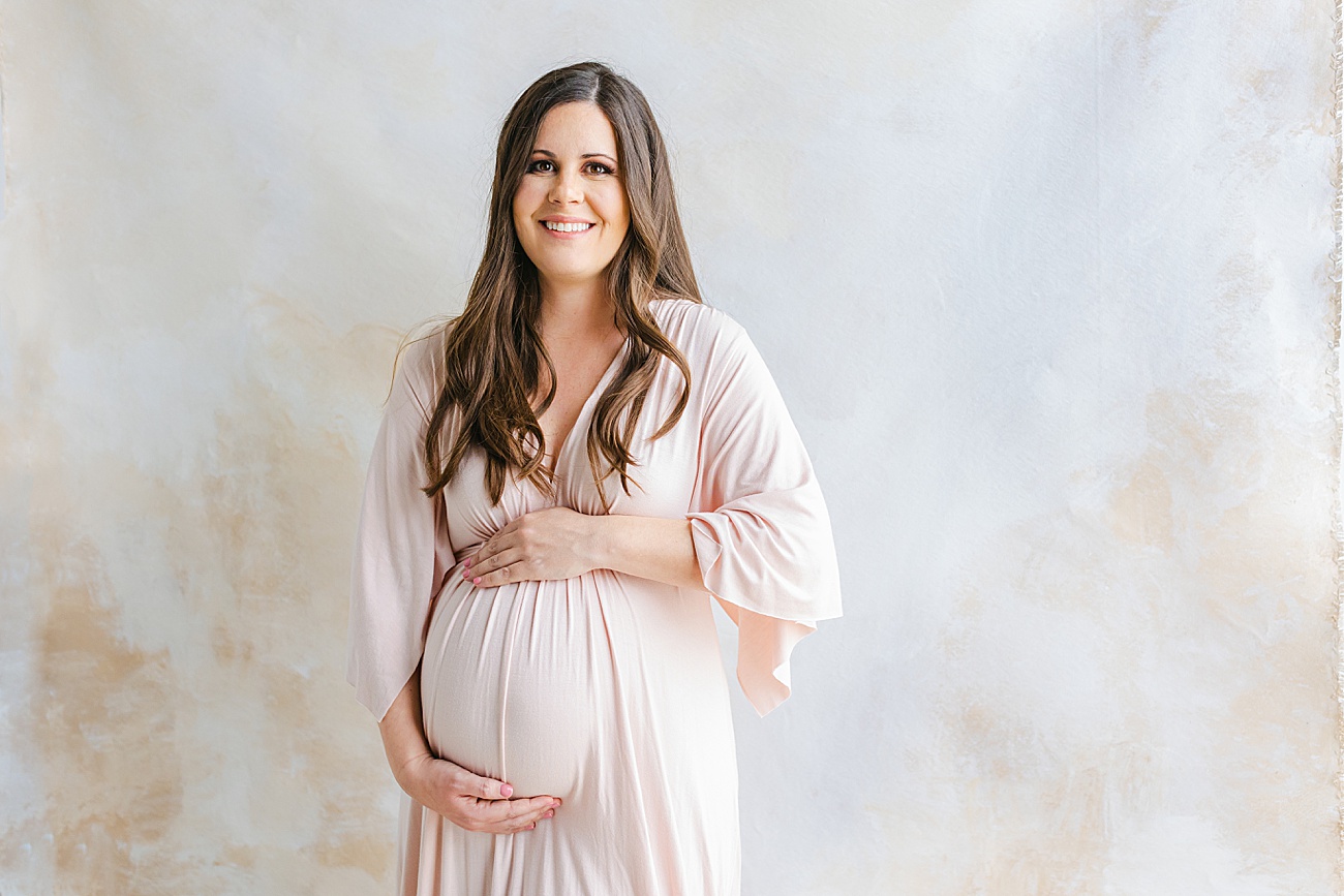 Beautiful Mama-to-be wearing blush maxi dress with hand-painted backdrop in Austin studio. Photo by Sana Ahmed Photography.