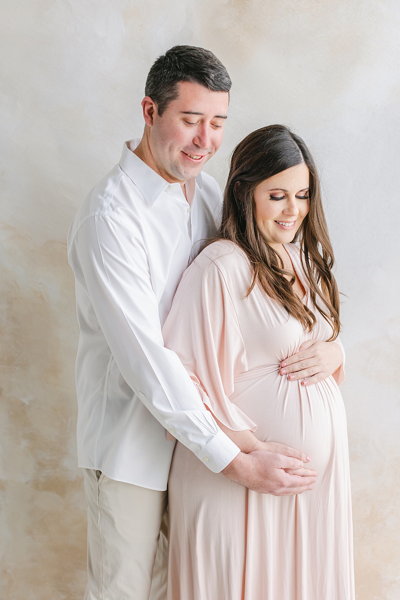 Expecting Mom and Dad hugging baby bump during studio maternity photos in Austin, TX. Photo by Sana Ahmed Photography.