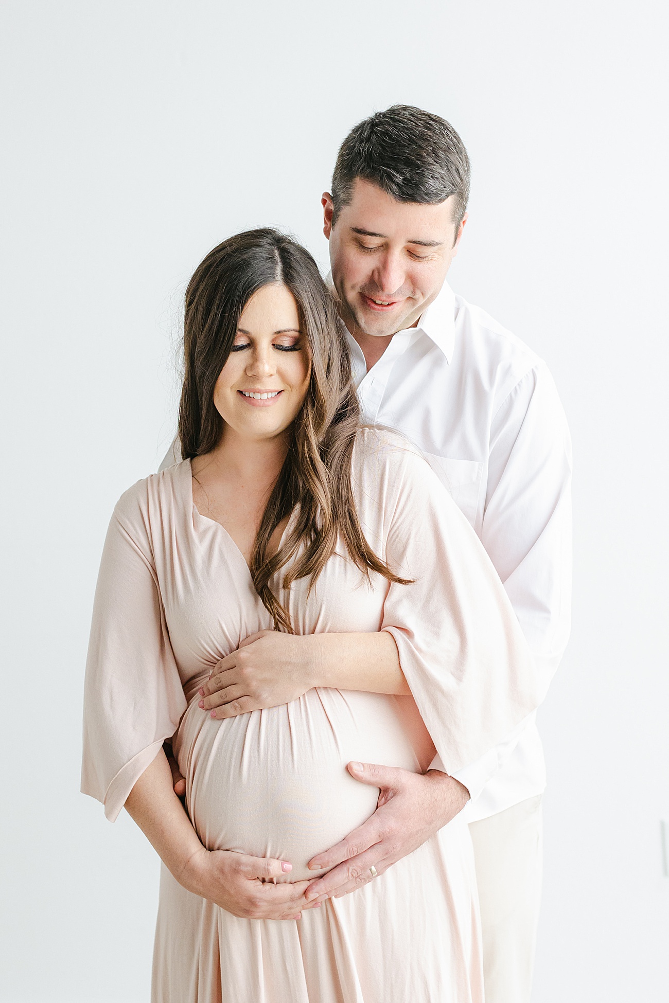 Sweet maternity pose as Dad stands behind Mom and hugs baby bump. Photo by Sana Ahmed Photography.