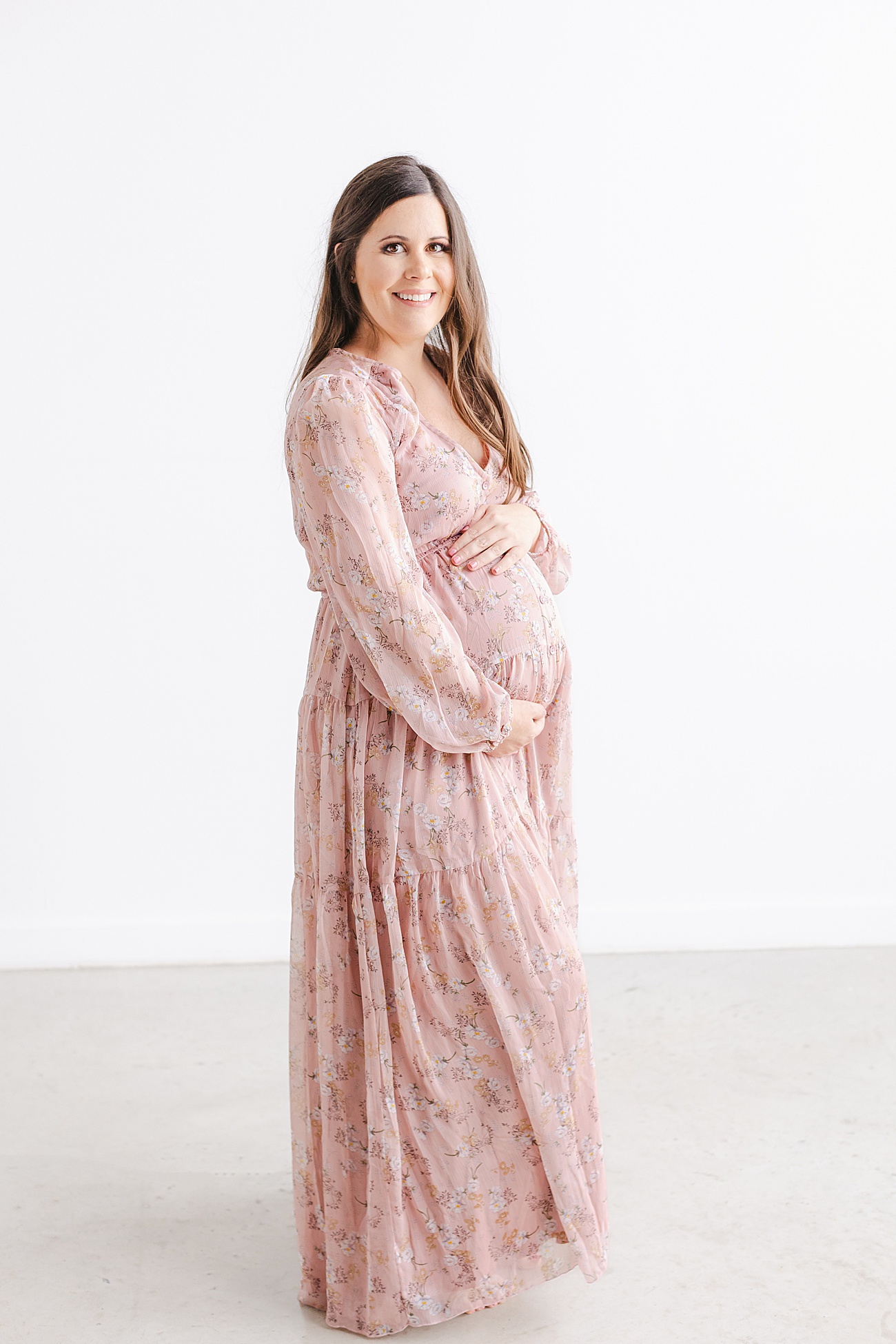 Beautiful Mama-to-be hugging baby bump while wearing pink floral maxi dress. Photo by Sana Ahmed Photography.