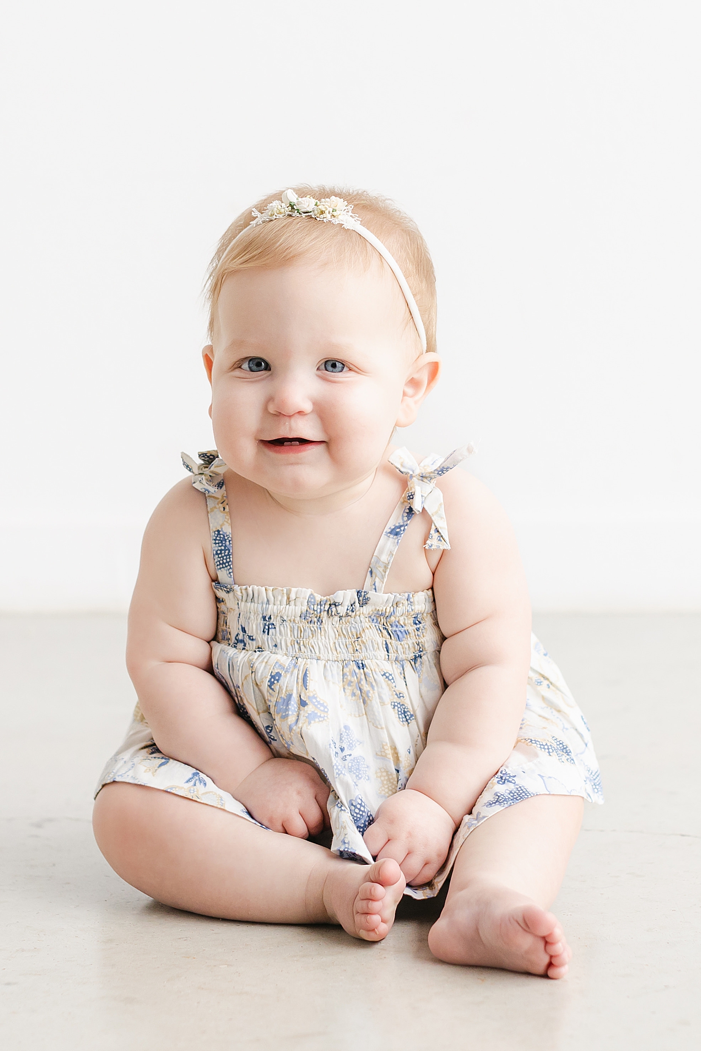 Baby girl in a cream and blue dress sitting and smiling | Sana Ahmed Photography