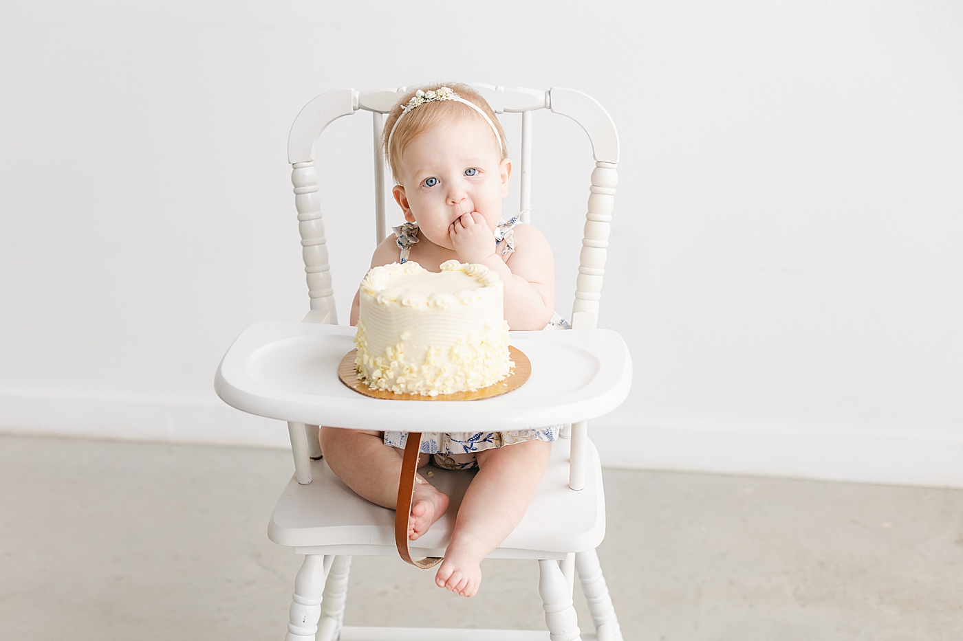 Baby girl in a headband eating cake during her one year milestone session | Sana Ahmed Photography