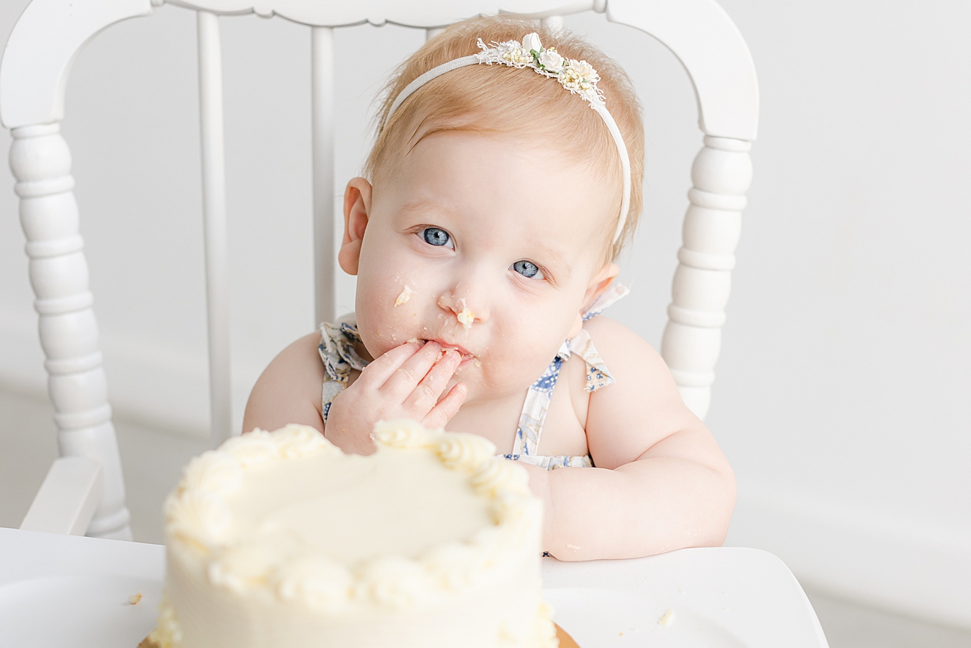 Baby girl in a highchair eating cake during her one year milestone session | Sana Ahmed Photography