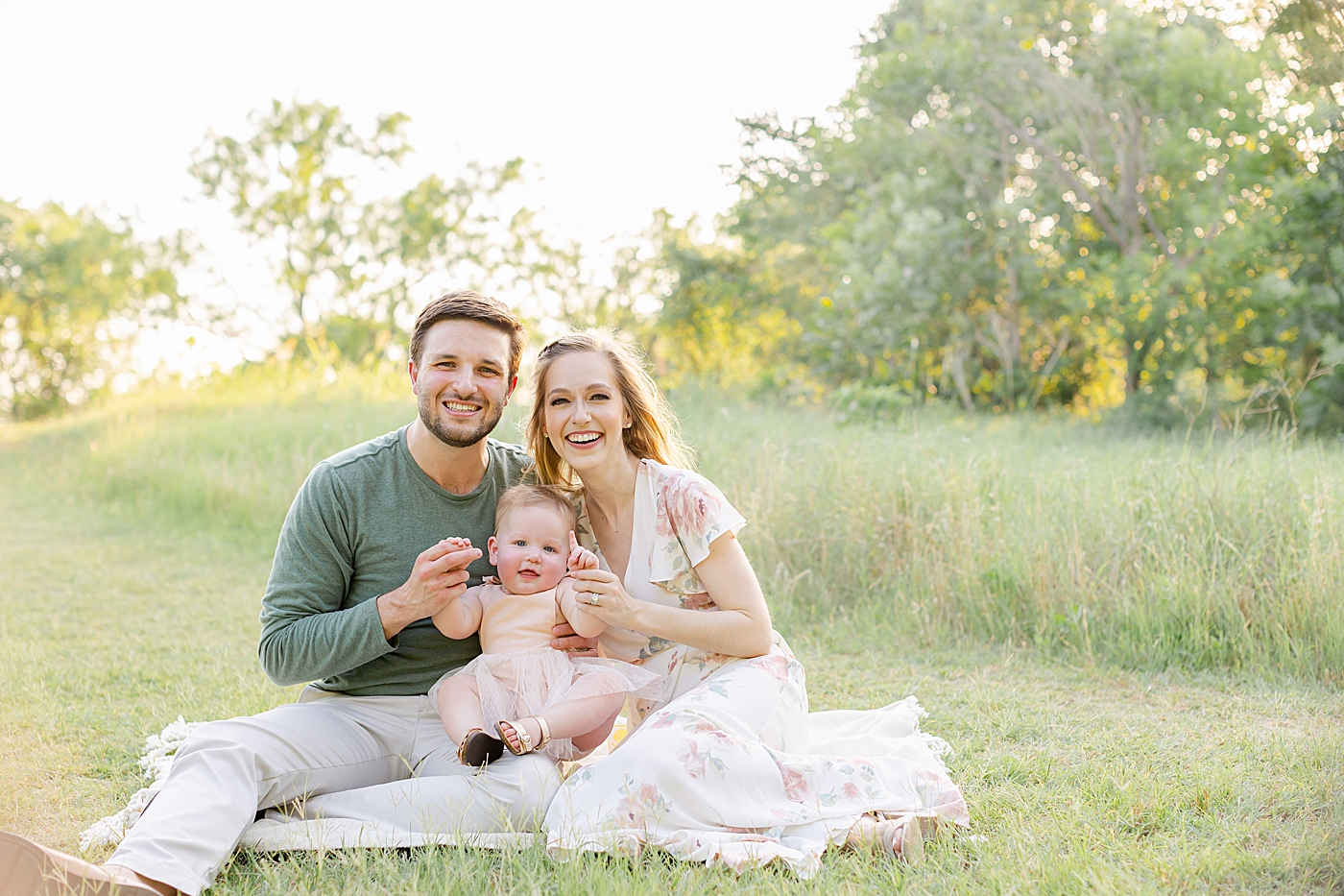 Mom and dad sitting on a blanket with their baby girl in a field | Sana Ahmed Photography