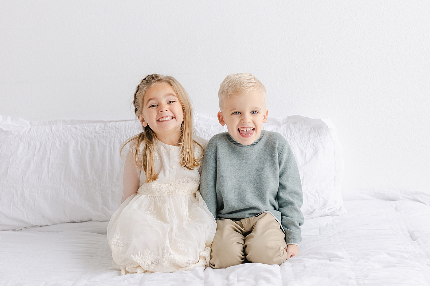Brother and sister giggling sitting on a bed | Photo by Sana Ahmed Photography