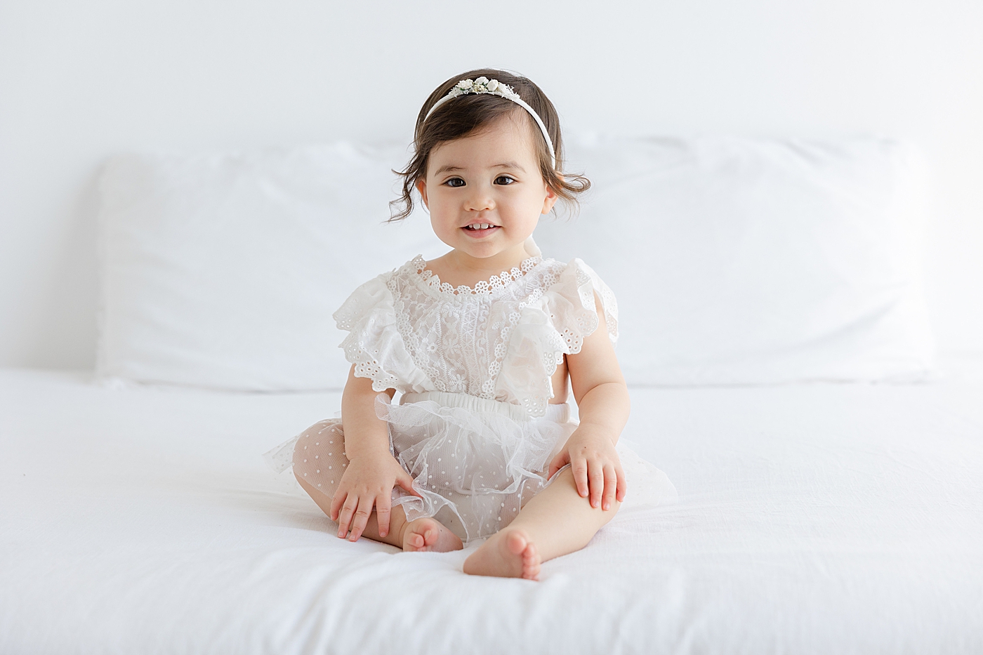 Baby girl in a white headband and dress smiling | Image by Sana Ahmed Photography