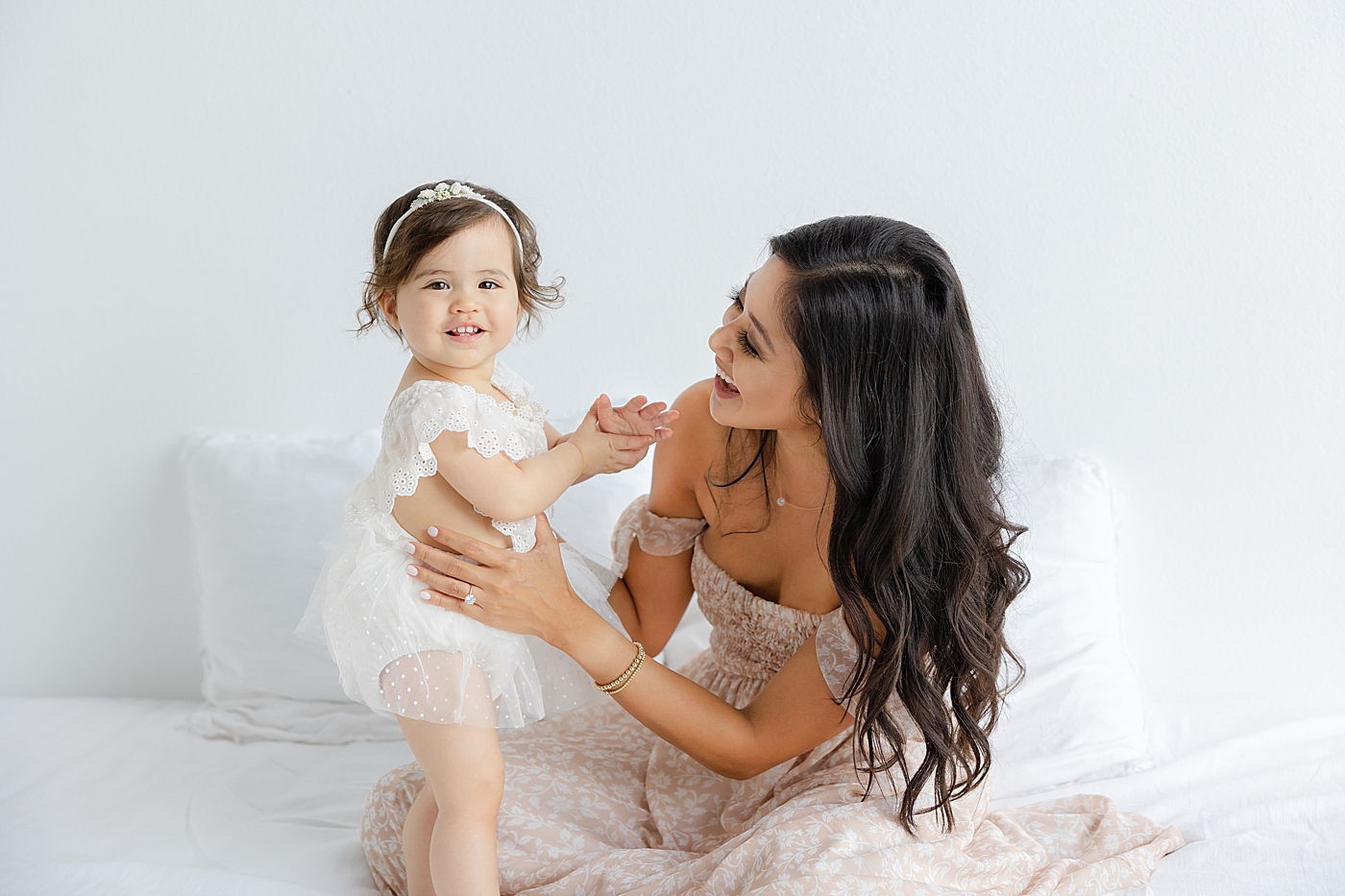 Mom and baby girl interacting sitting on a bed | Image by Sana Ahmed Photography