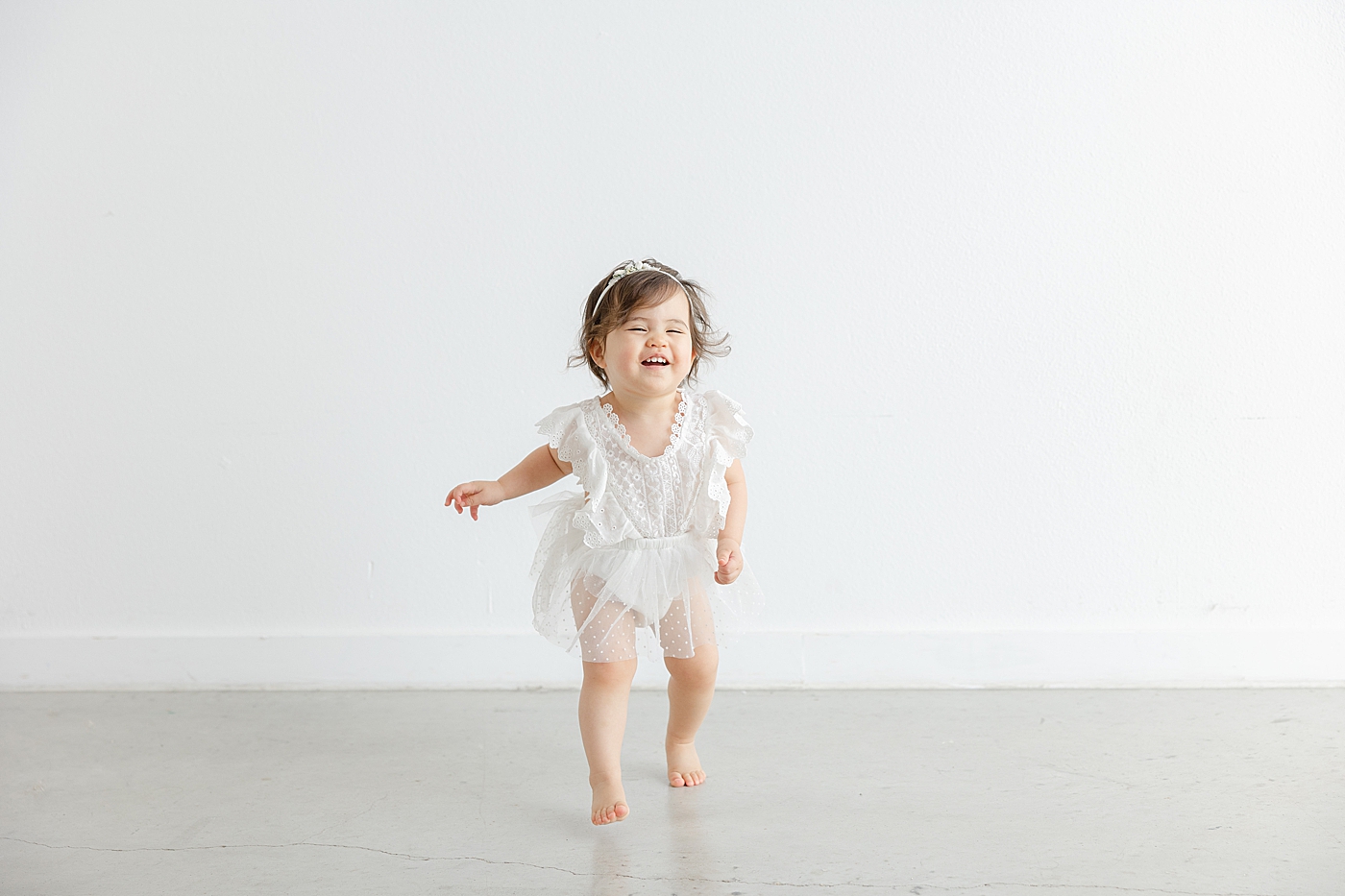 Baby girl in a white dress walking in the studio during her one year studio milestone session | Image by Sana Ahmed Photography
