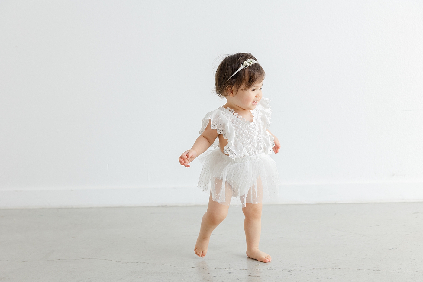 Baby girl in a white dress walking in the studio | Image by Sana Ahmed Photography