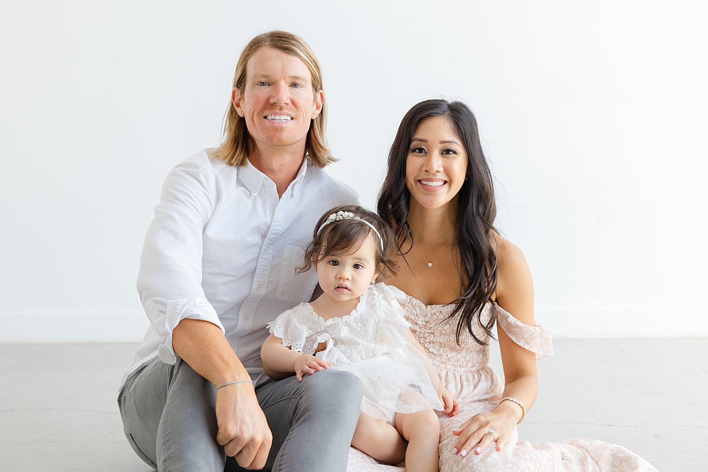 Mom, dad, and baby girl sitting on the floor during her one year studio milestone session| Image by Sana Ahmed Photography
