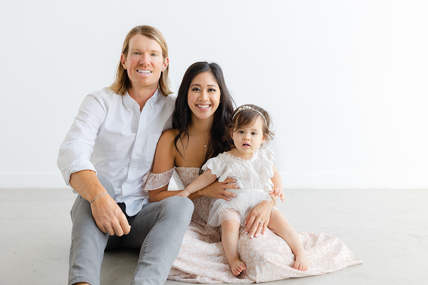 Mom and dad sitting on the floor with their baby girl during her one year studio milestone session| Image by Sana Ahmed Photography
