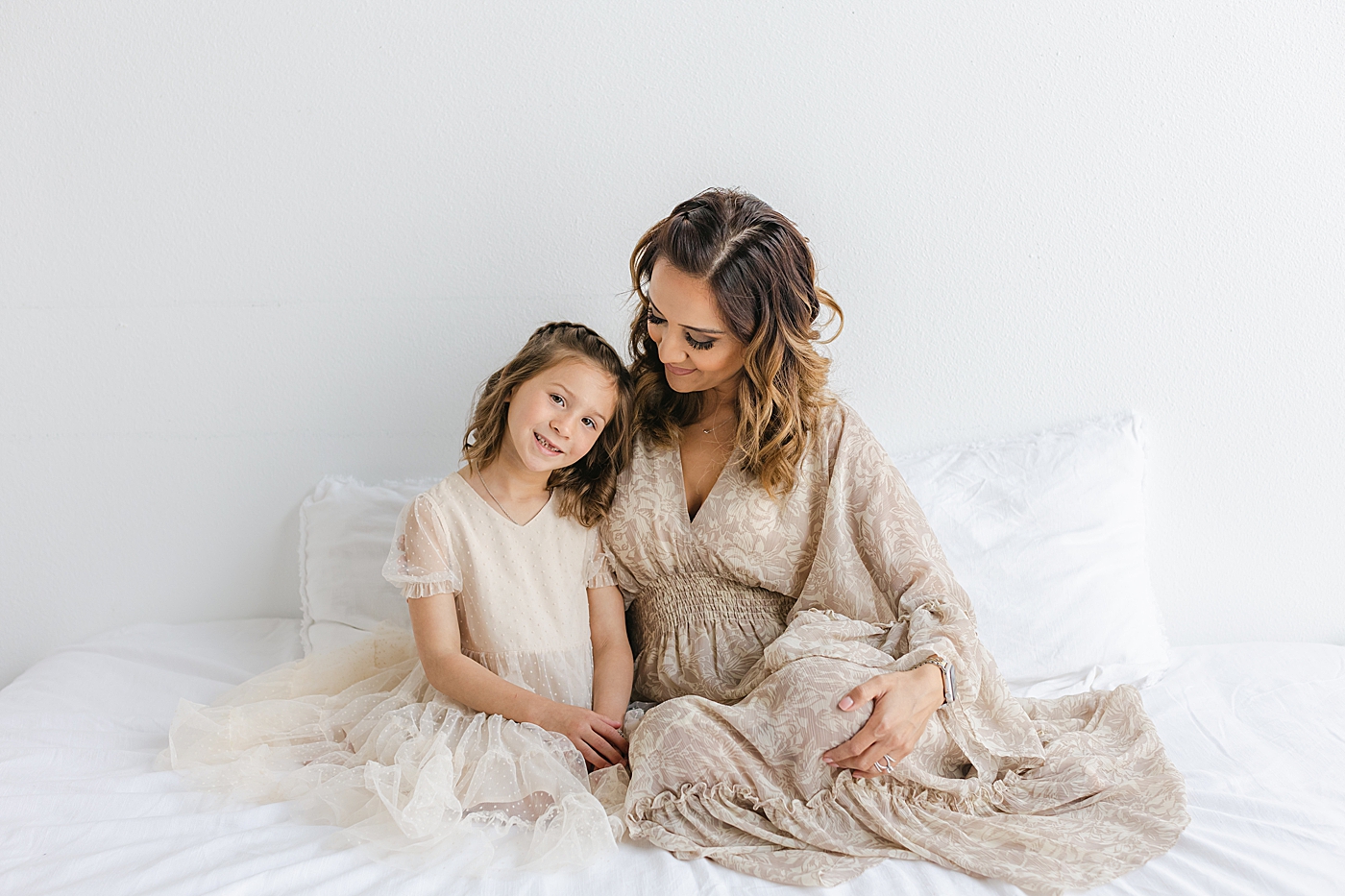 Mom and daughter sitting together on a white bed | Photo by Sana Ahmed Photography