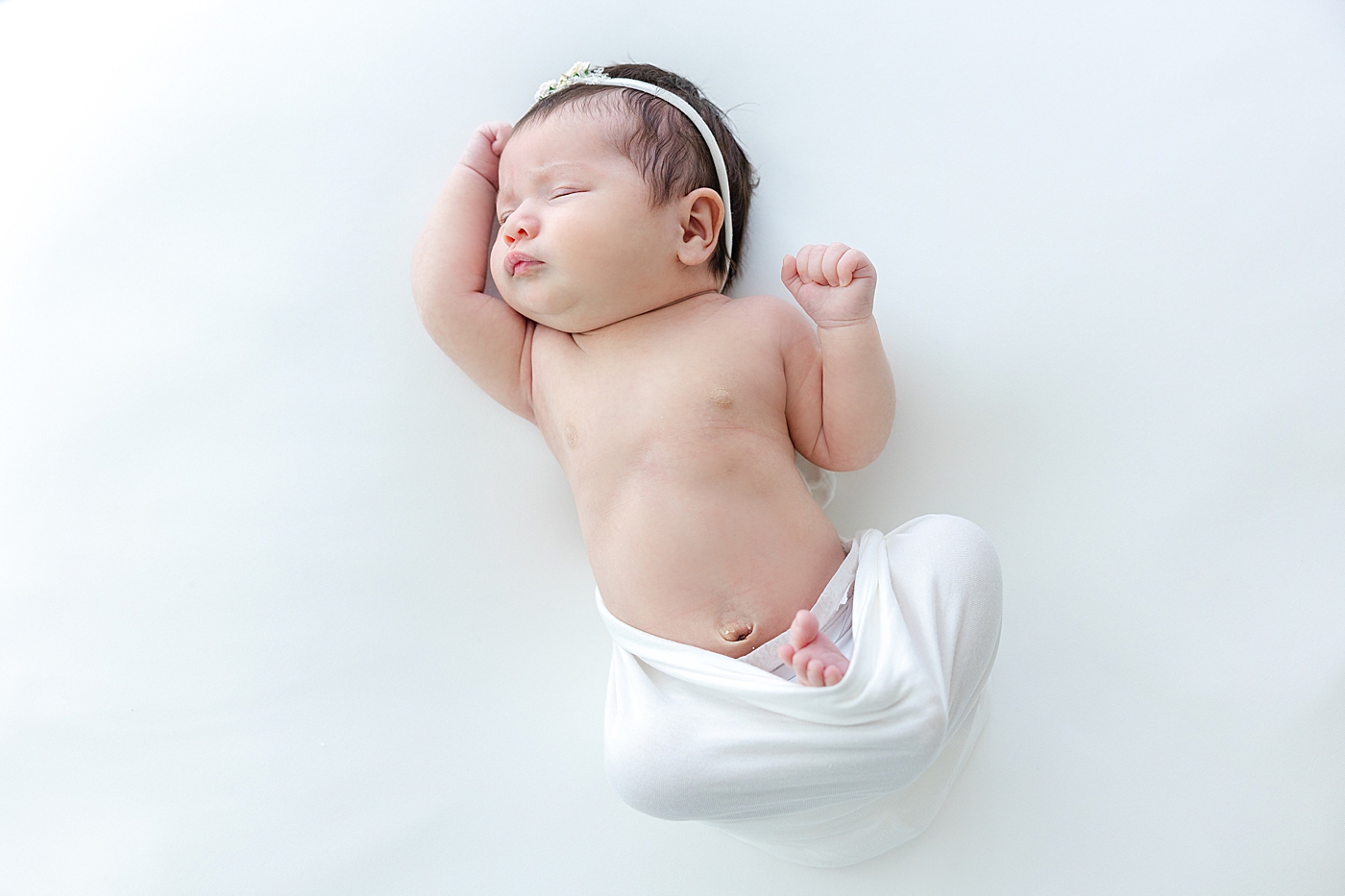 Sleeping newborn stretching wrapped in white swaddle during her Austin Studio Newborn Session | Photo by Sana Ahmed Photography
