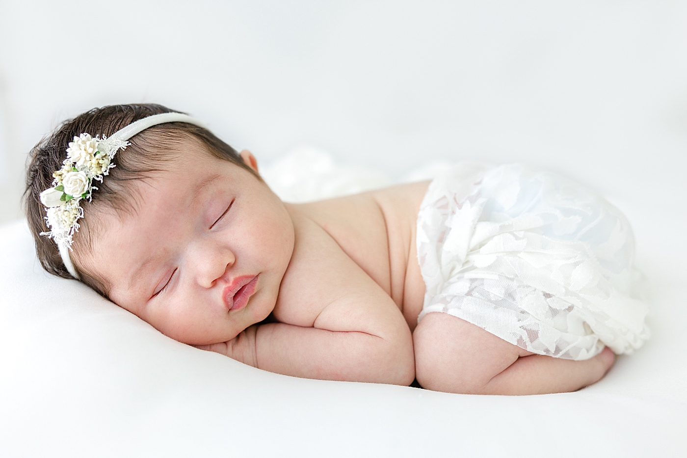 Sleeping newborn baby in white bloomers and headband | Photo by Sana Ahmed Photography