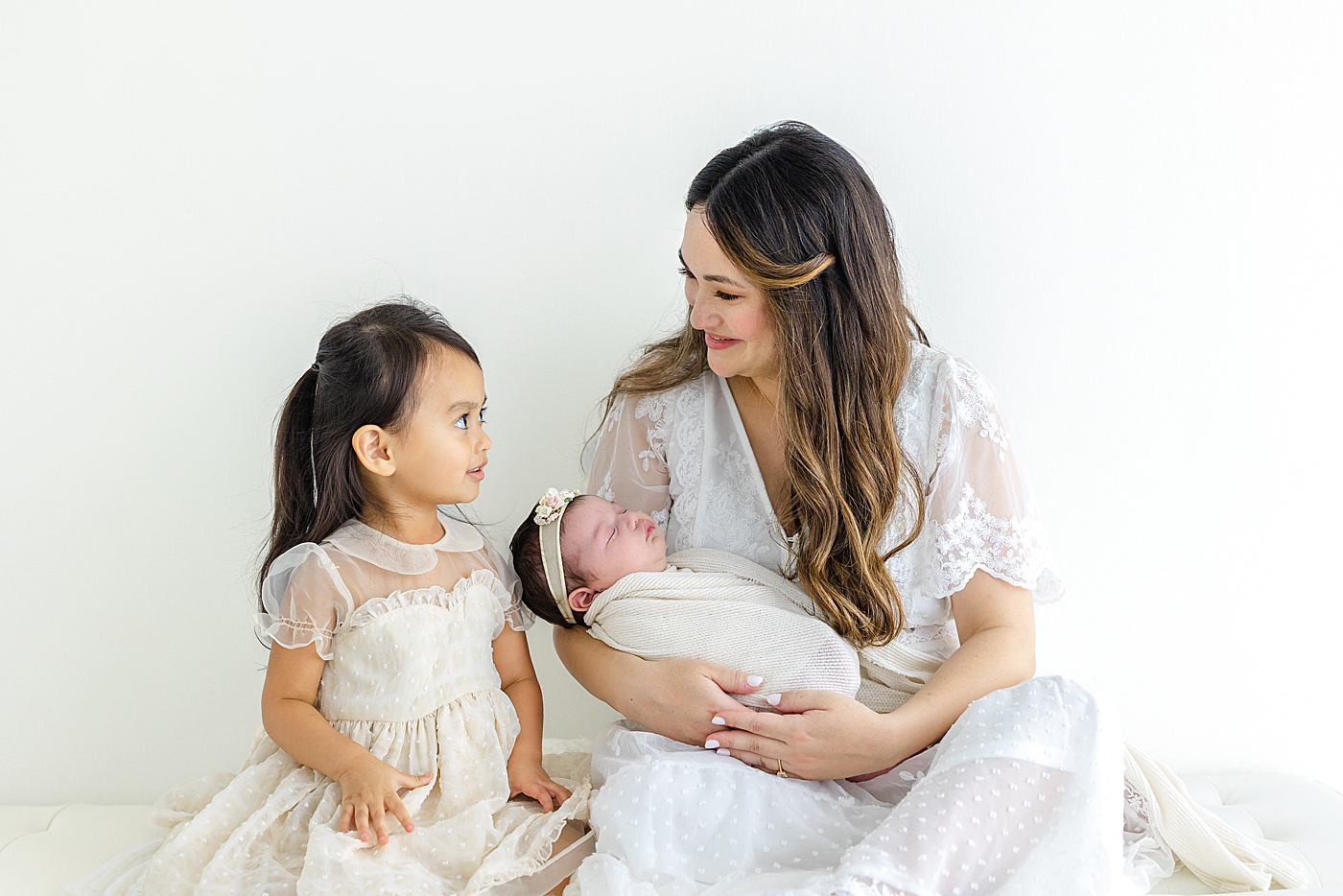 Mom sitting with her two baby girls in white | Photo by Sana Ahmed Photography