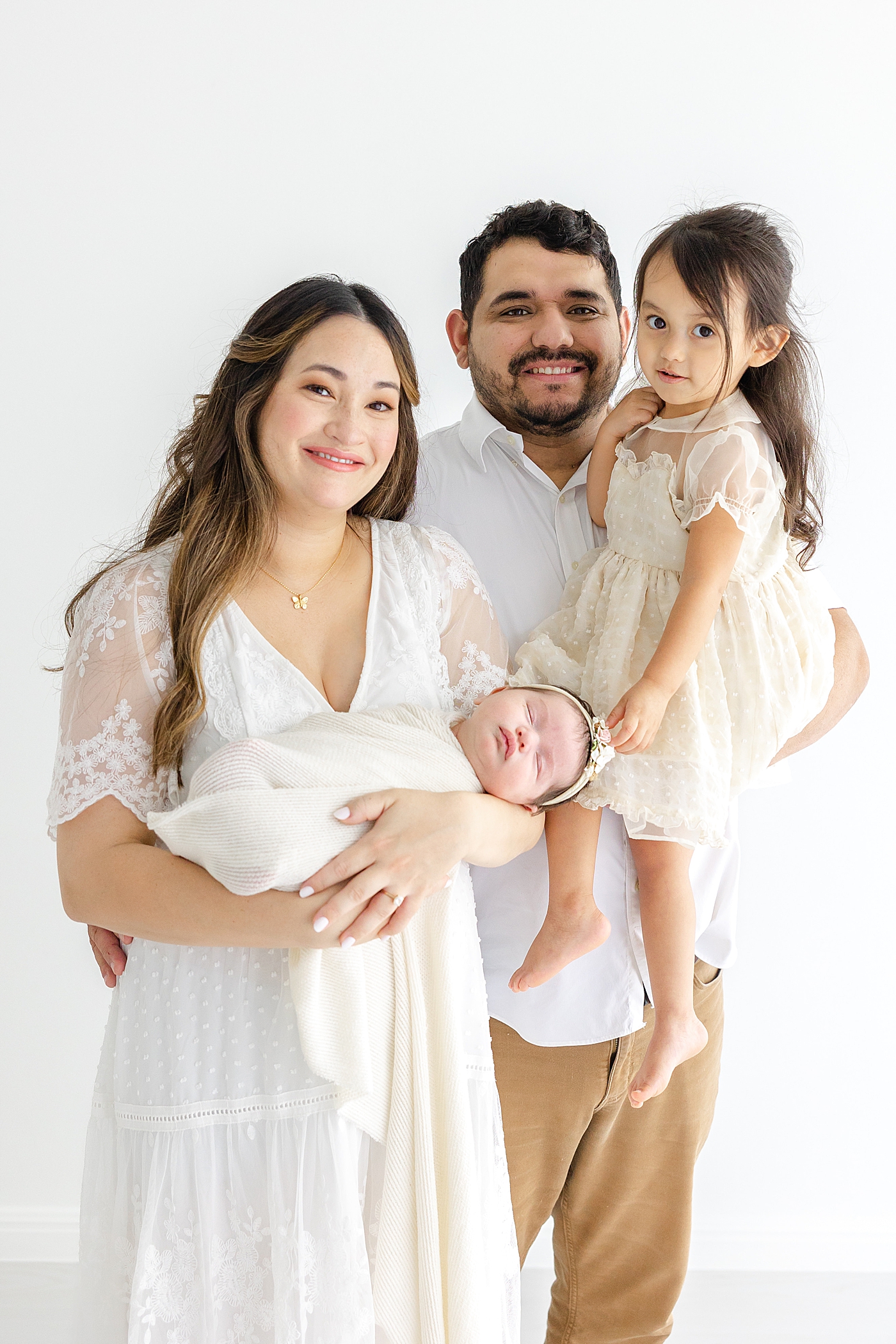 Mom and dad holding their kids during her Austin Studio Newborn Session | Photo by Sana Ahmed Photography