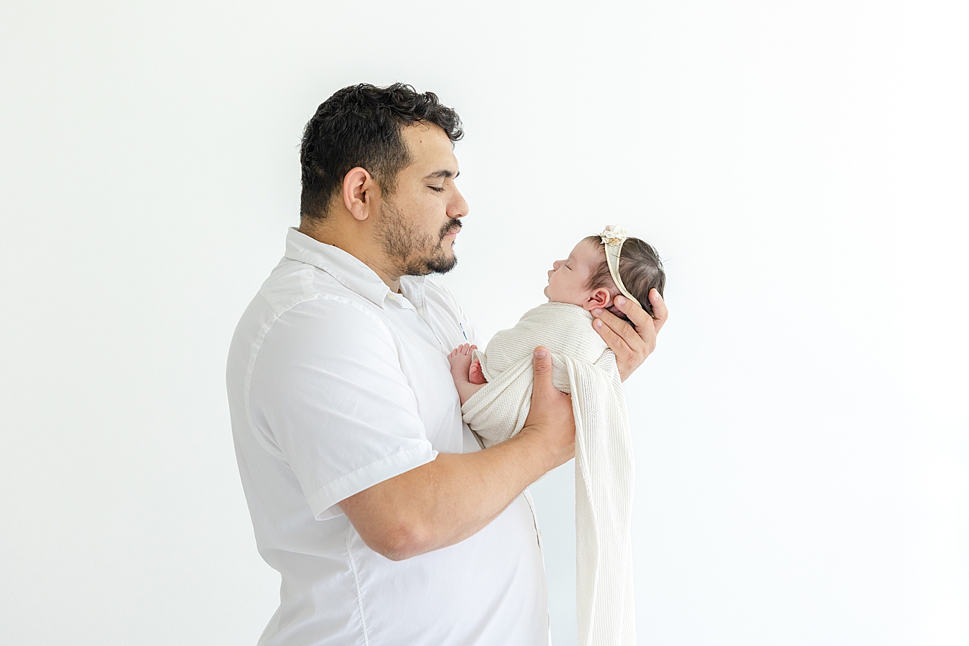 Dad holding his newborn baby girl wrapped in a white swaddle | Photo by Sana Ahmed Photography