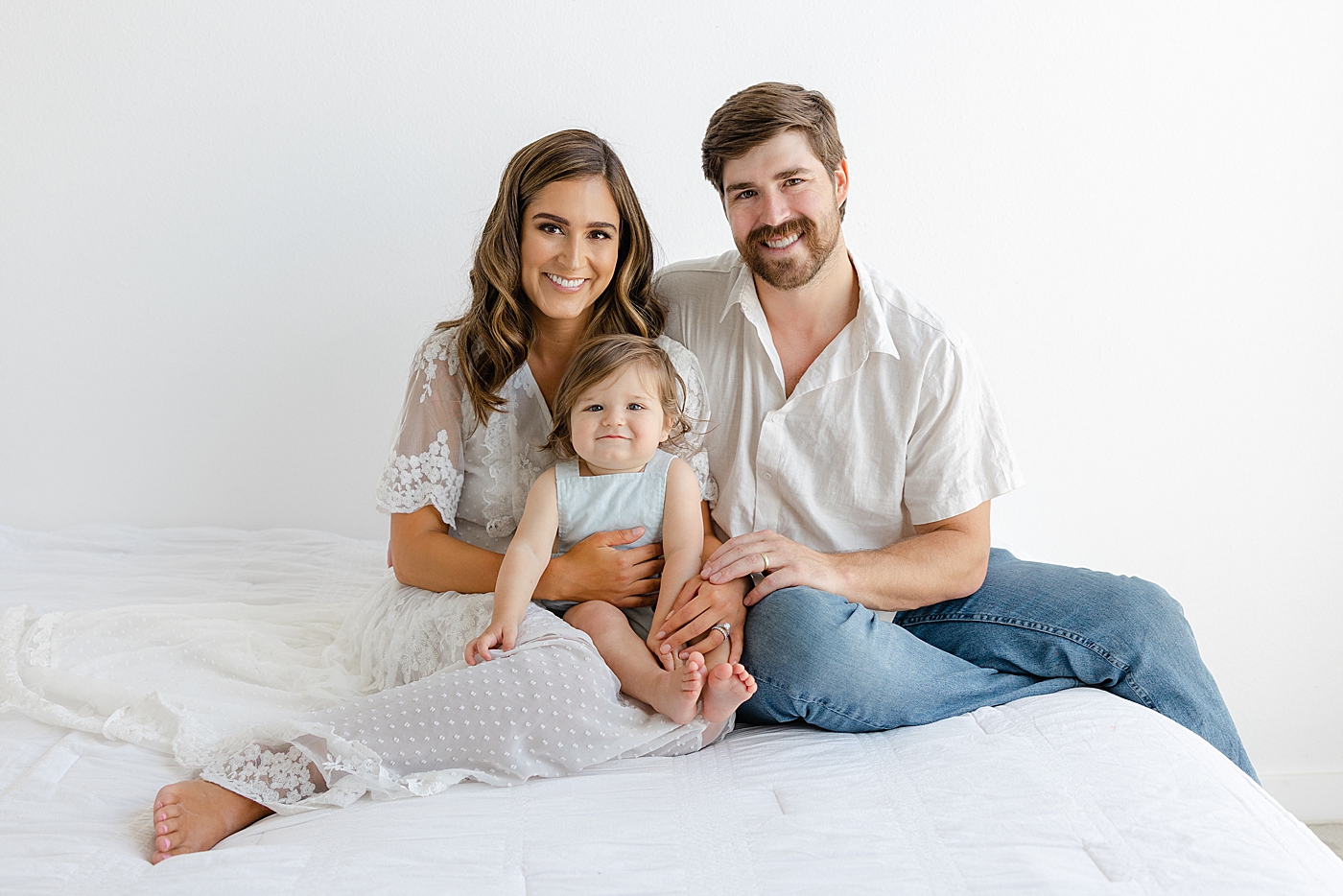 Mom and dad sitting on a bed with their baby during their Studio Family Session | Photo by Sana Ahmed Photography