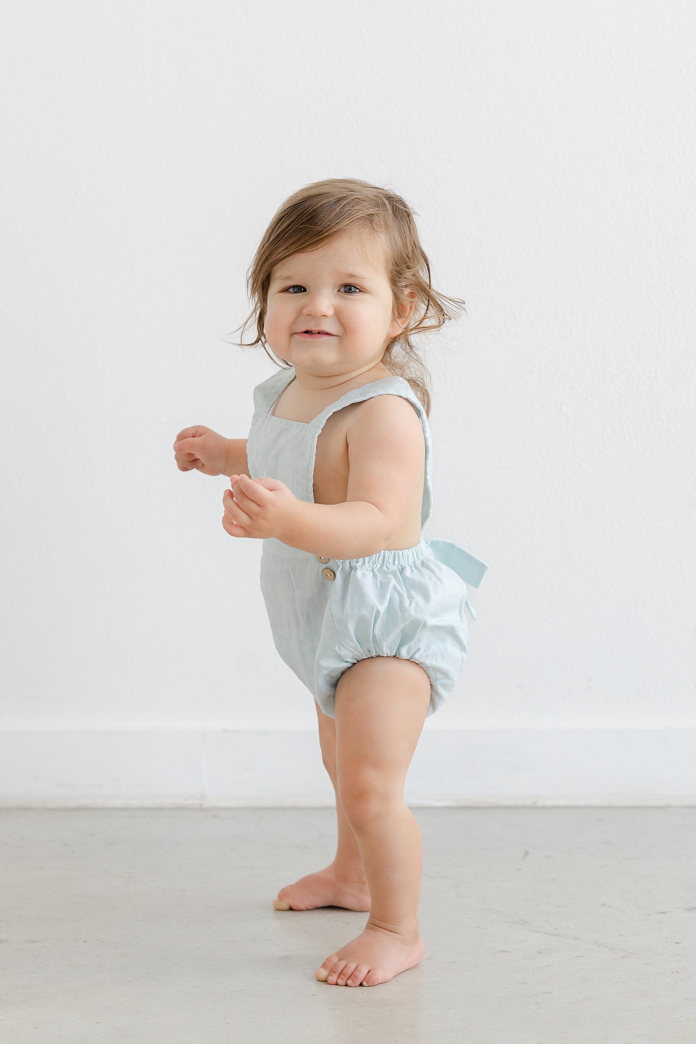 Baby girl in a light blue romper standing | Photo by Sana Ahmed Photography