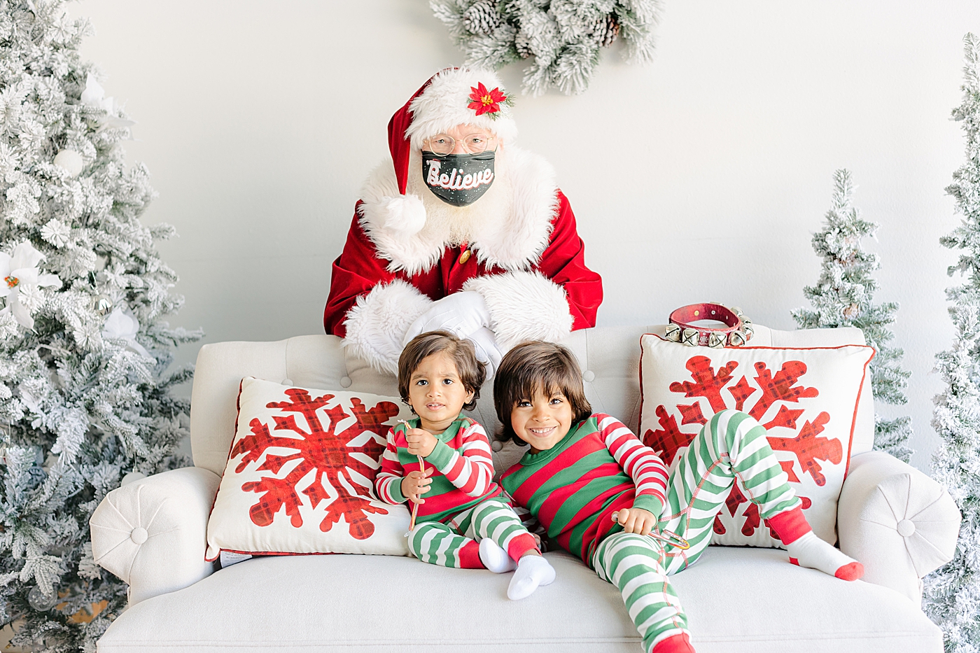 Brothers in Christmas pajamas sitting on a couch with Santa in the background | Images by Sana Ahmed Photography