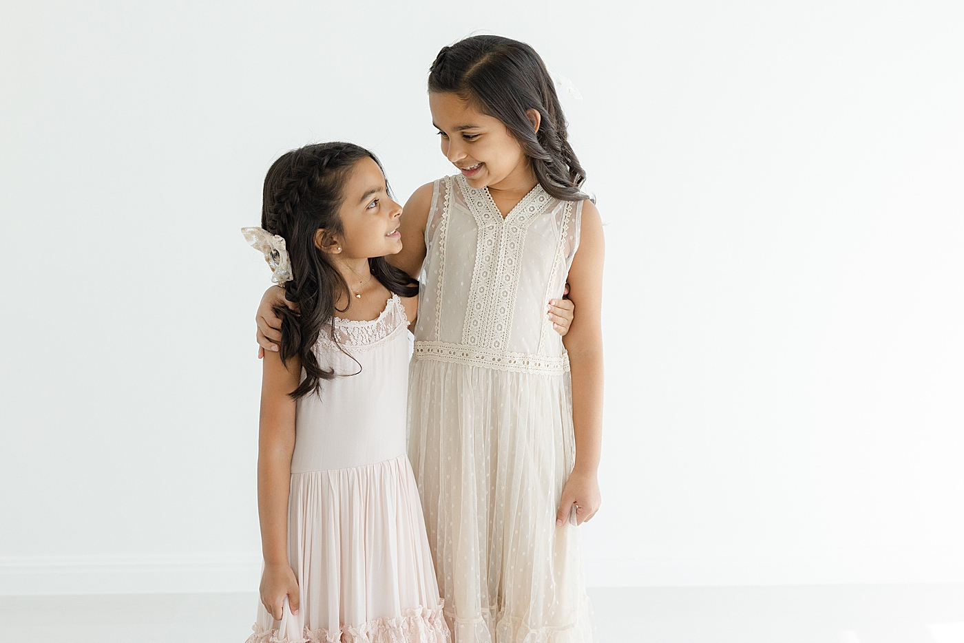 Two sisters in long neutral dresses hugging | Image by Sana Ahmed Photography