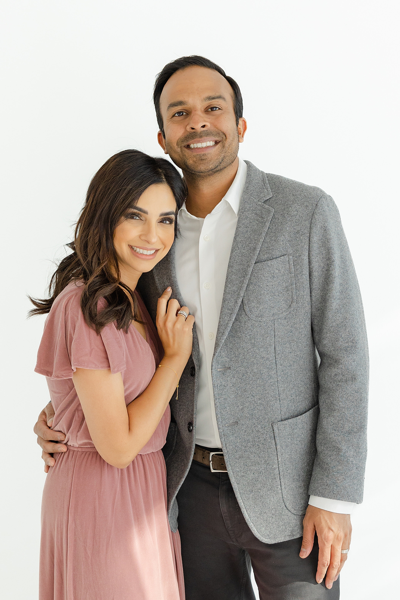 Mom and dad in pink and gray snuggling in the studio | Image by Sana Ahmed Photography