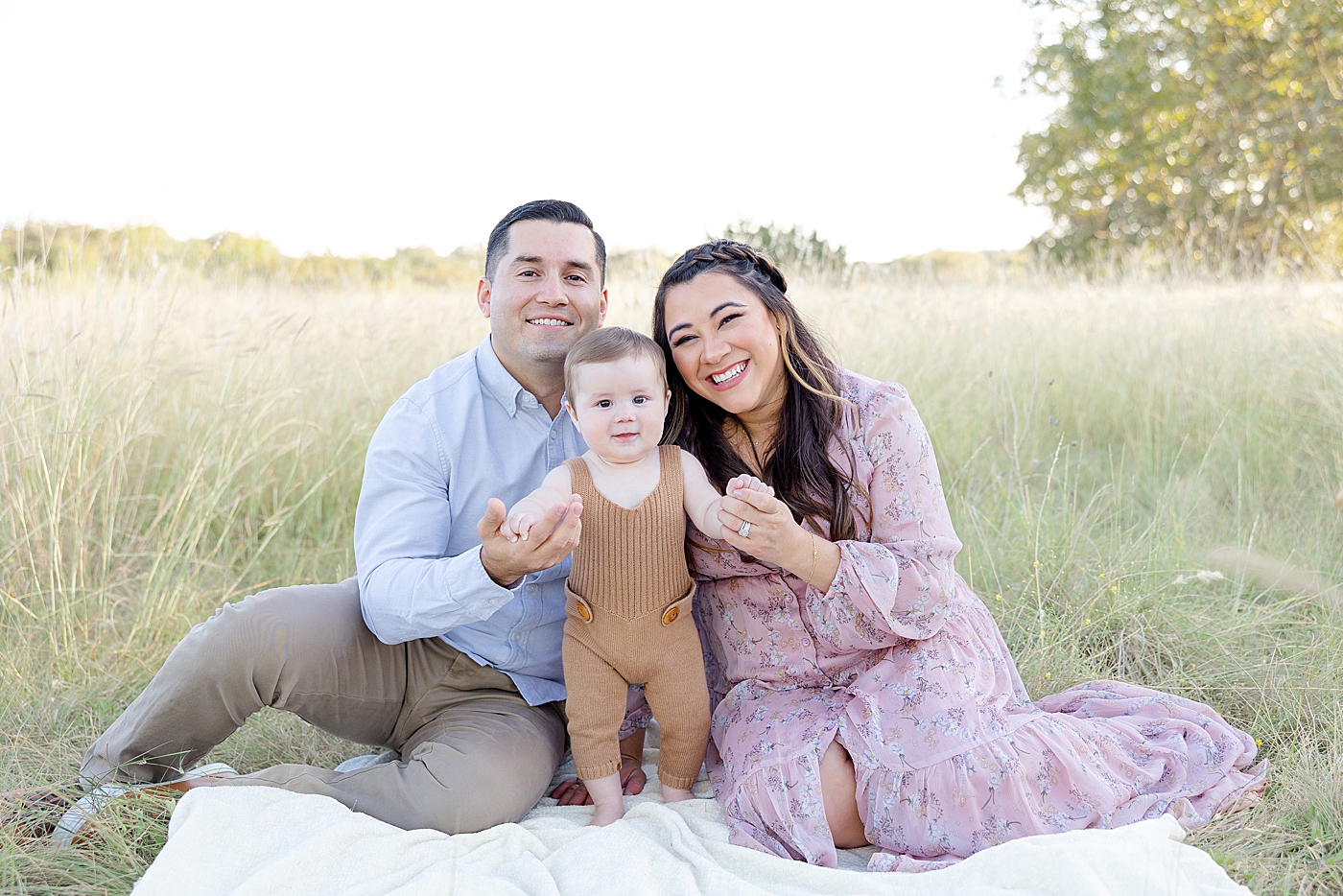 Family of three sitting in the grass during their session | Image by Sana Ahmed Photography