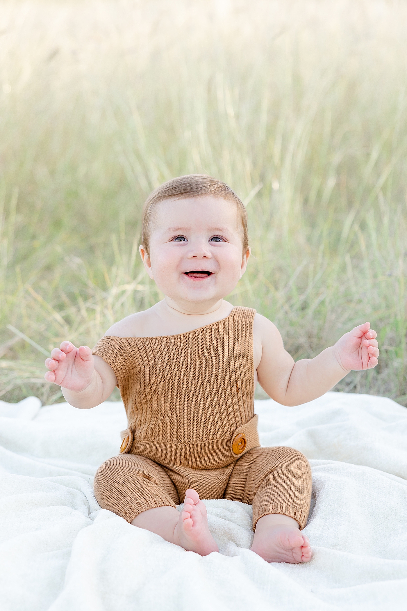 Smiling baby boy sitting on a blanket in the grass | Image by Sana Ahmed Photography
