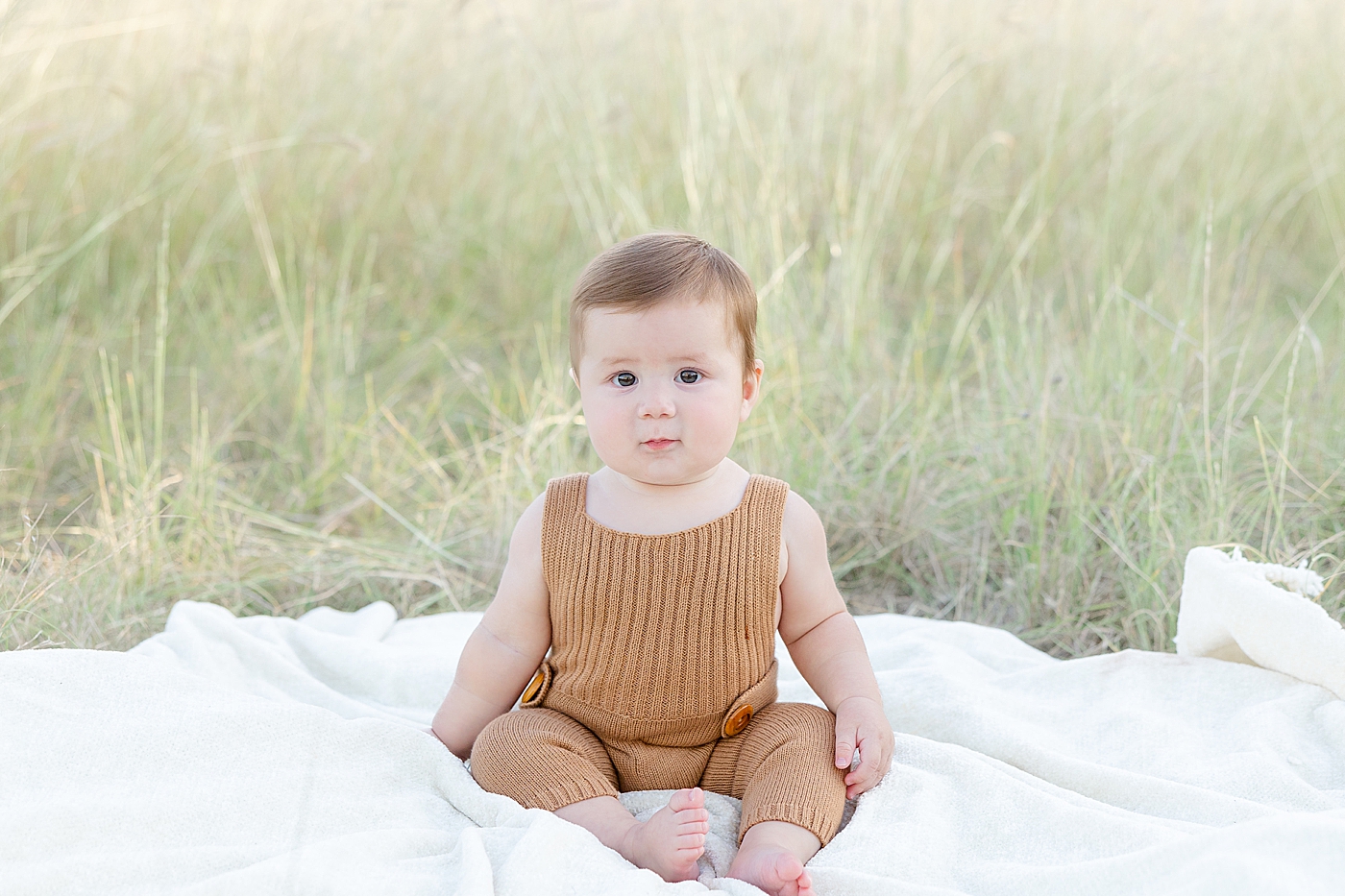 Baby boy in brown jumpsuit sitting in the grass | Image by Sana Ahmed Photography