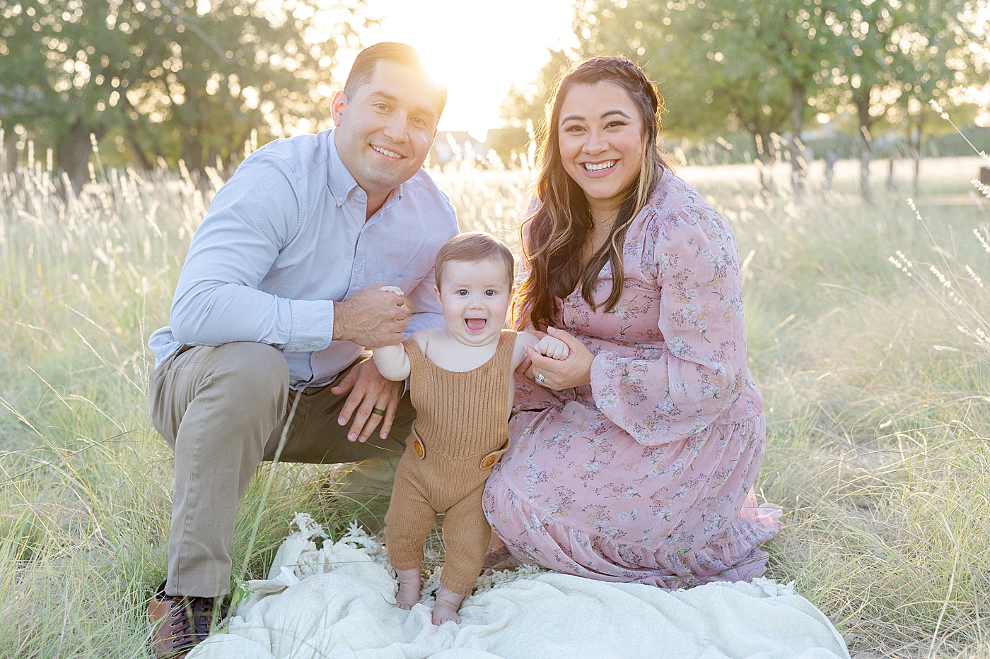 Mom and dad sitting in the grass with their baby during Six Month Milestone Session | Image by Sana Ahmed Photography