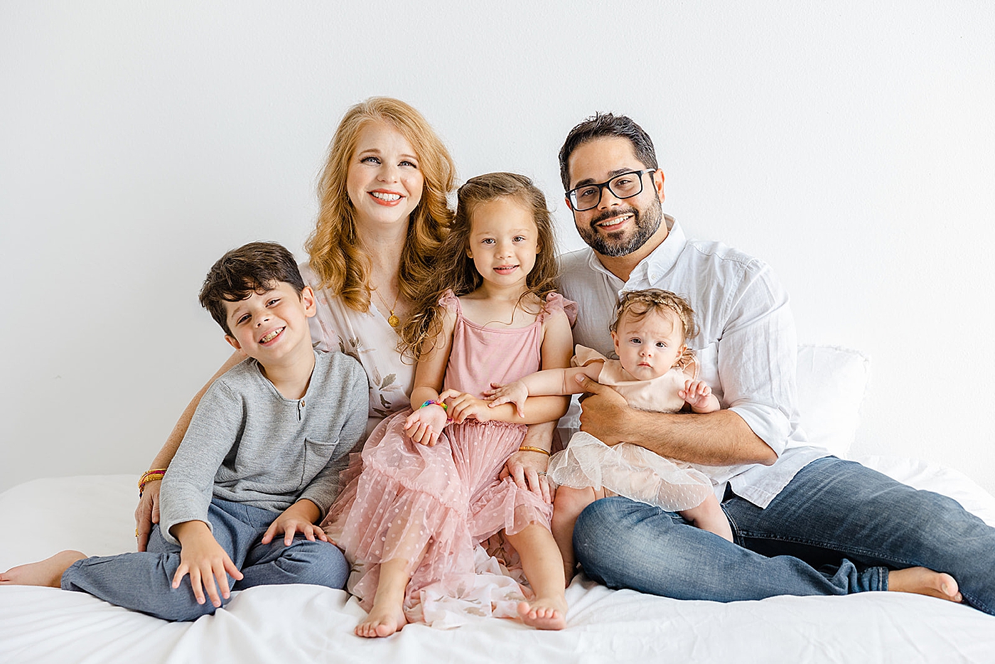 Family of five sitting on a bed smiling | Studio Family Sessions Austin with Sana Ahmed Photography