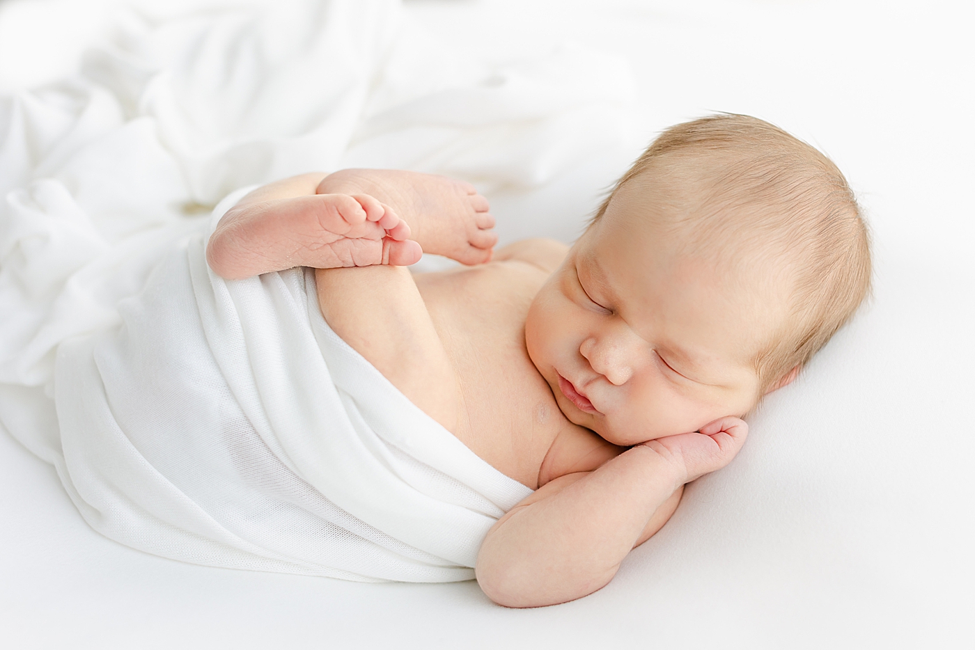 Newborn baby boy sleeping while wrapped in a white swaddle | Image by Sana Ahmed Photography 
