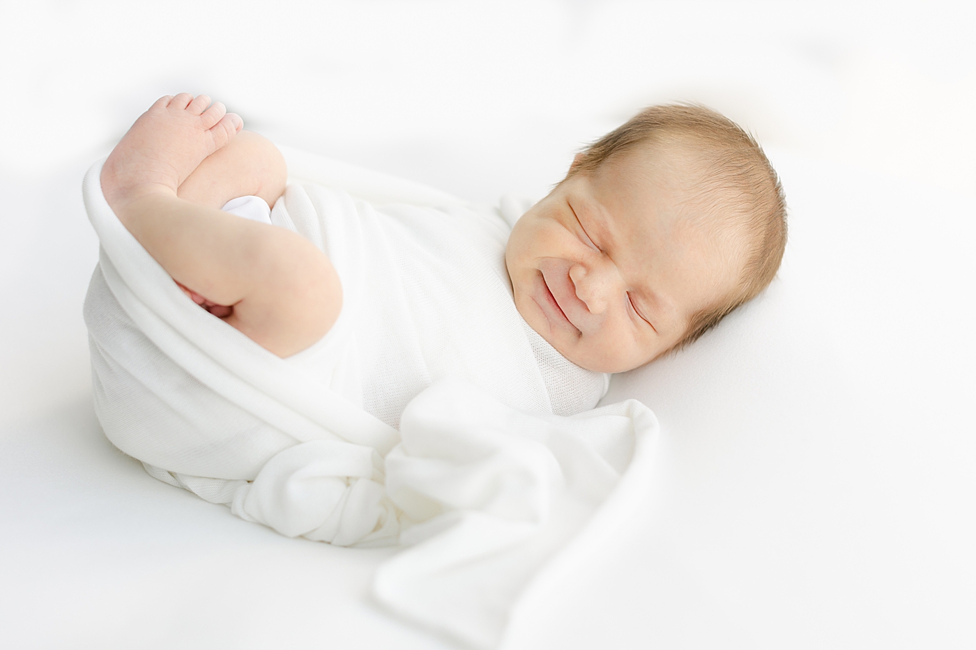 Smiling newborb baby in a white swaddle | Image by Sana Ahmed Photography 